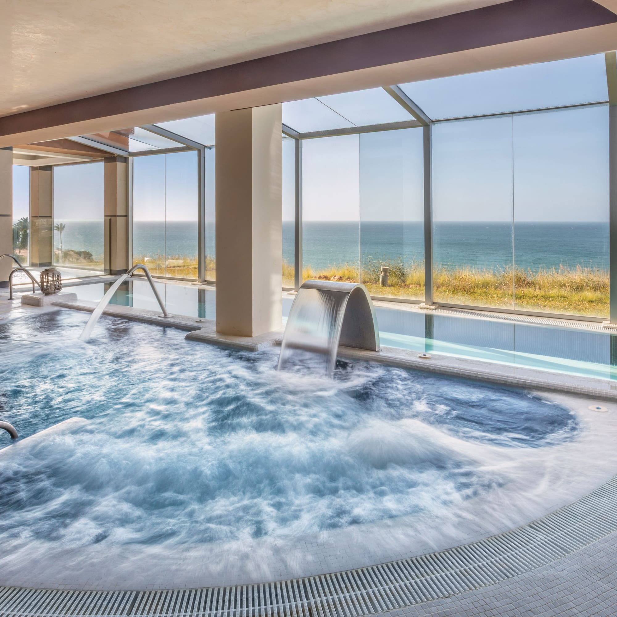 Modern indoor spa with jacuzzi, water features, and panoramic ocean view.