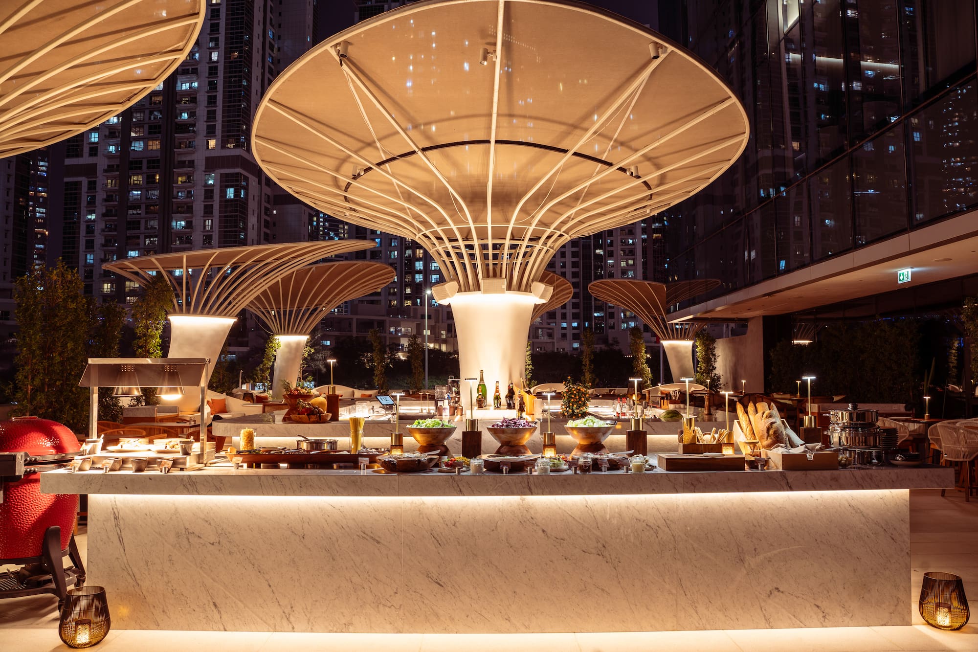 Outdoor luxury buffet with illuminated canopies and city skyline at night.