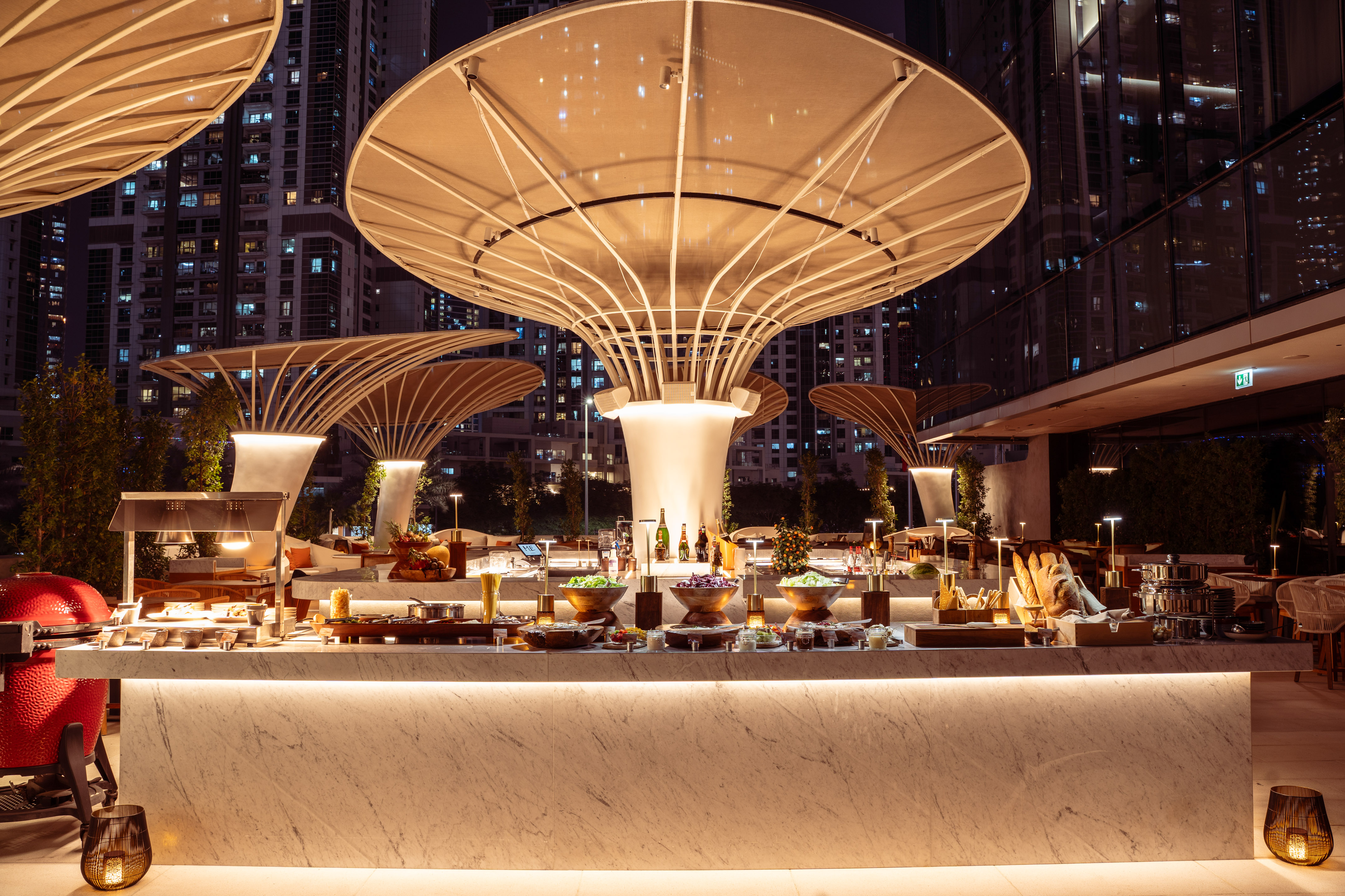 Outdoor luxury buffet with illuminated canopies and city skyline at night.
