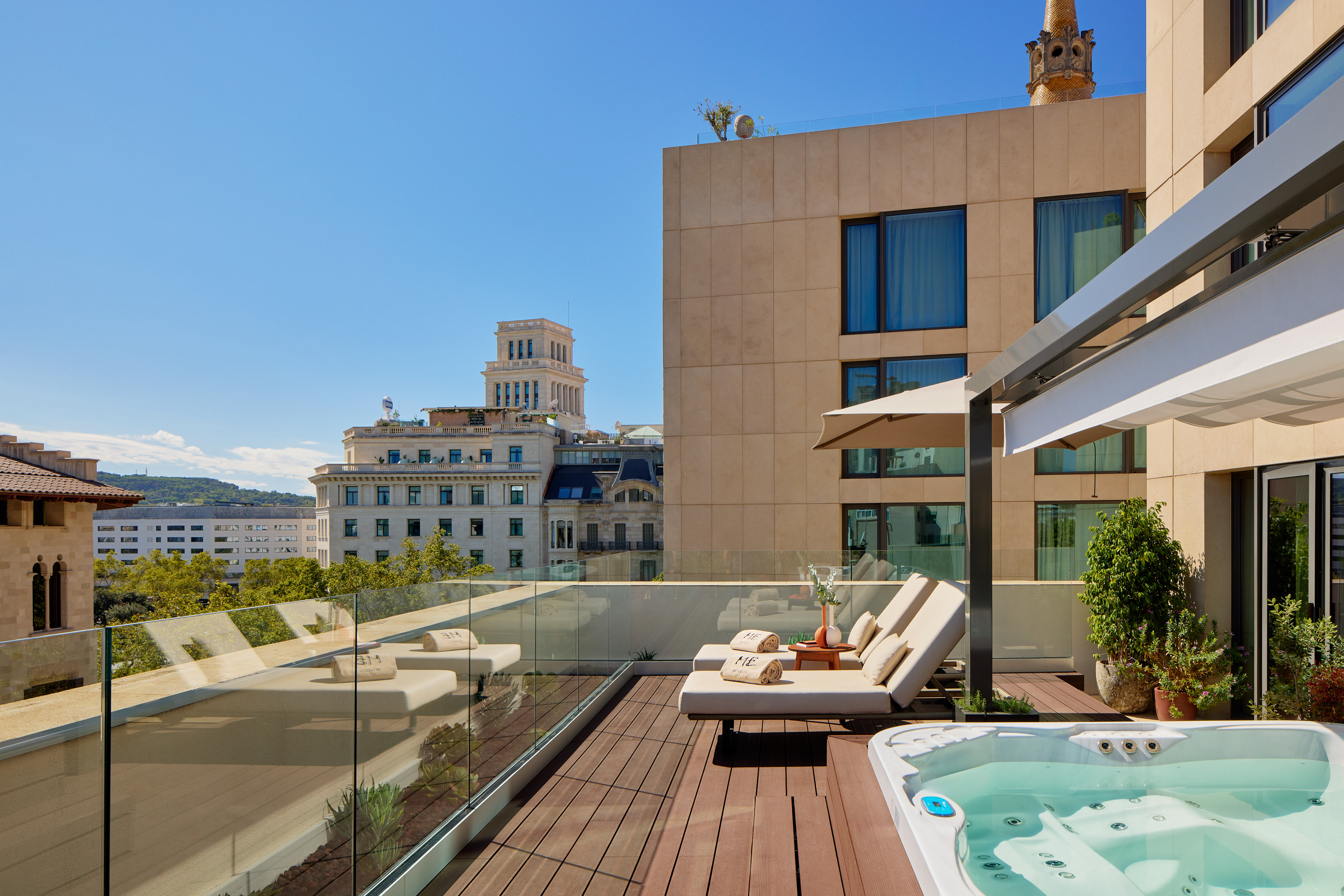 Hotel rooftop terrace with jacuzzi, lounge chairs, and city view.