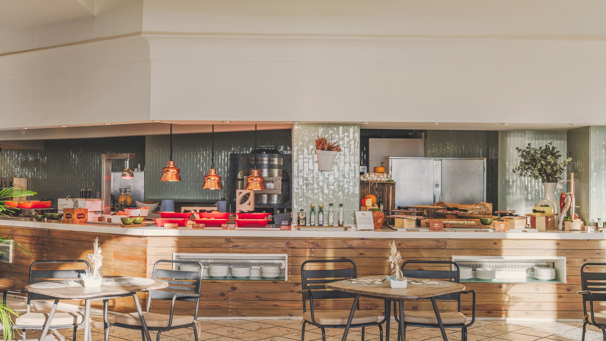 Bright buffet restaurant with food display, wooden counter, tables and chairs.