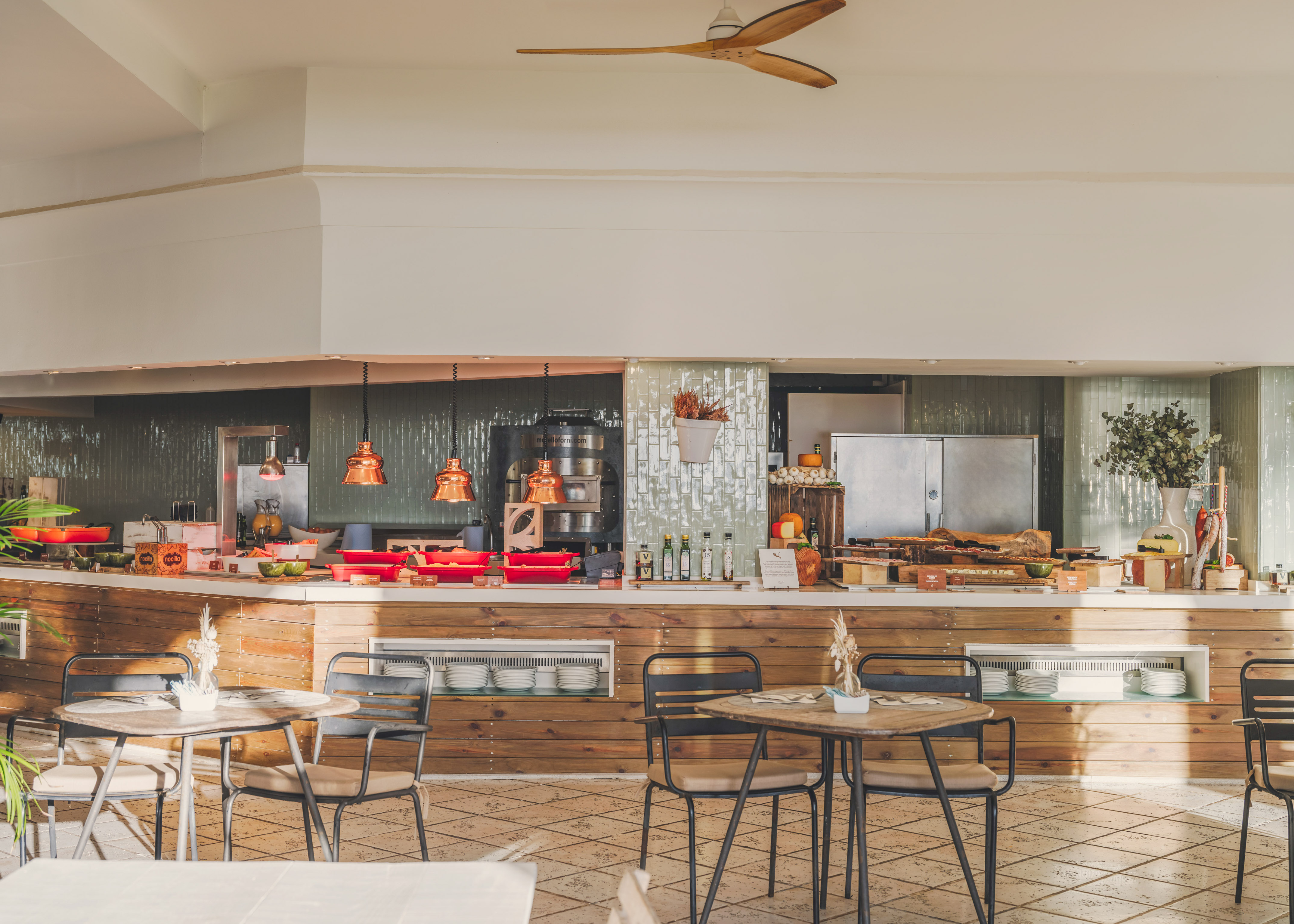 Bright buffet restaurant with food display, wooden counter, tables and chairs.