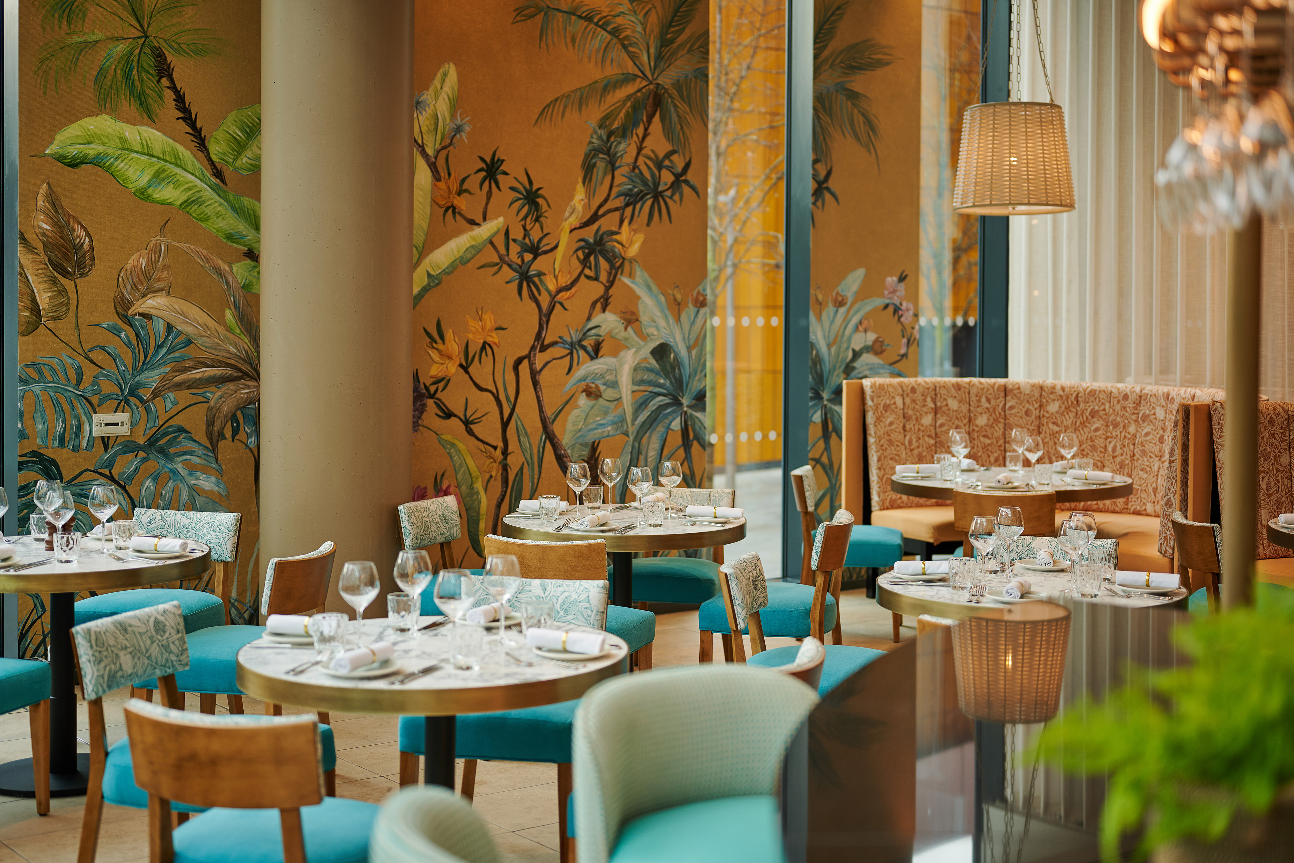 Tropical-themed restaurant interior with teal chairs and set tables.