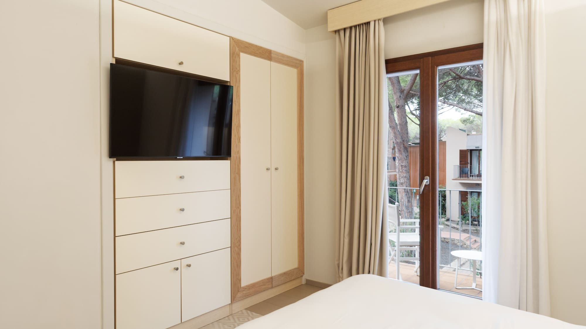 Clean bedroom with built-in TV, integrated storage, and balcony access.
