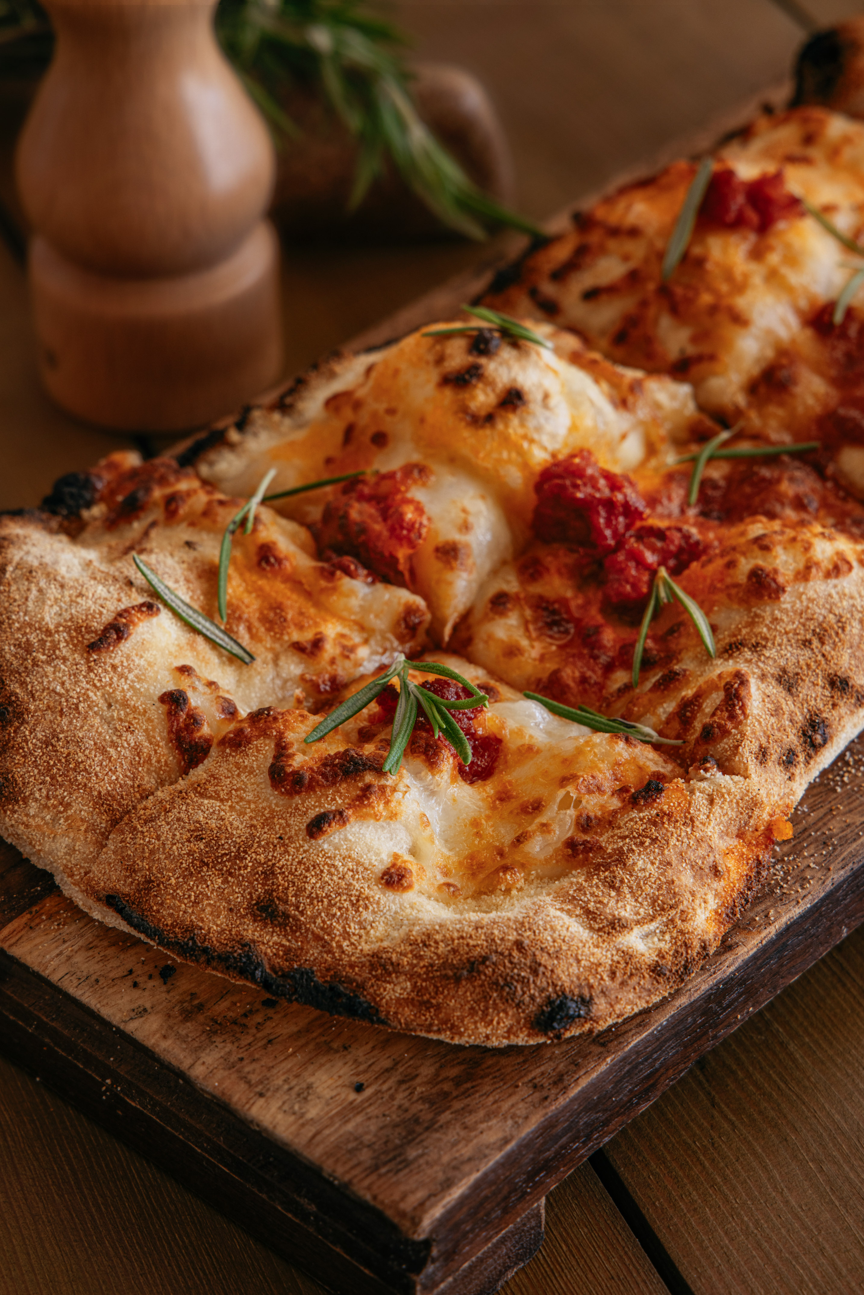 Artisan pizza with melted cheese, tomato, and fresh rosemary on wood.