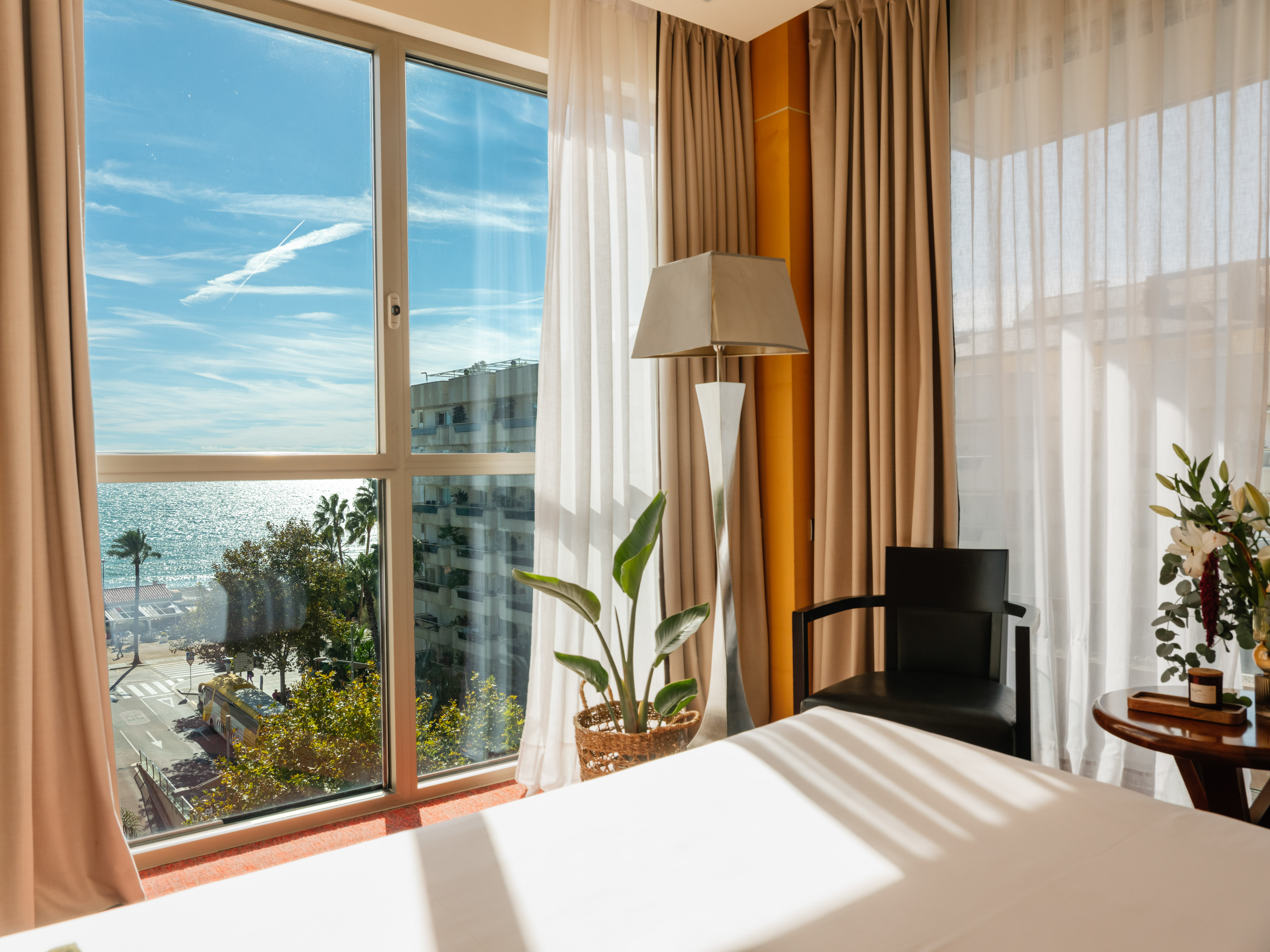 Hotel room with beachfront ocean view, large window, bed, and cozy decor.