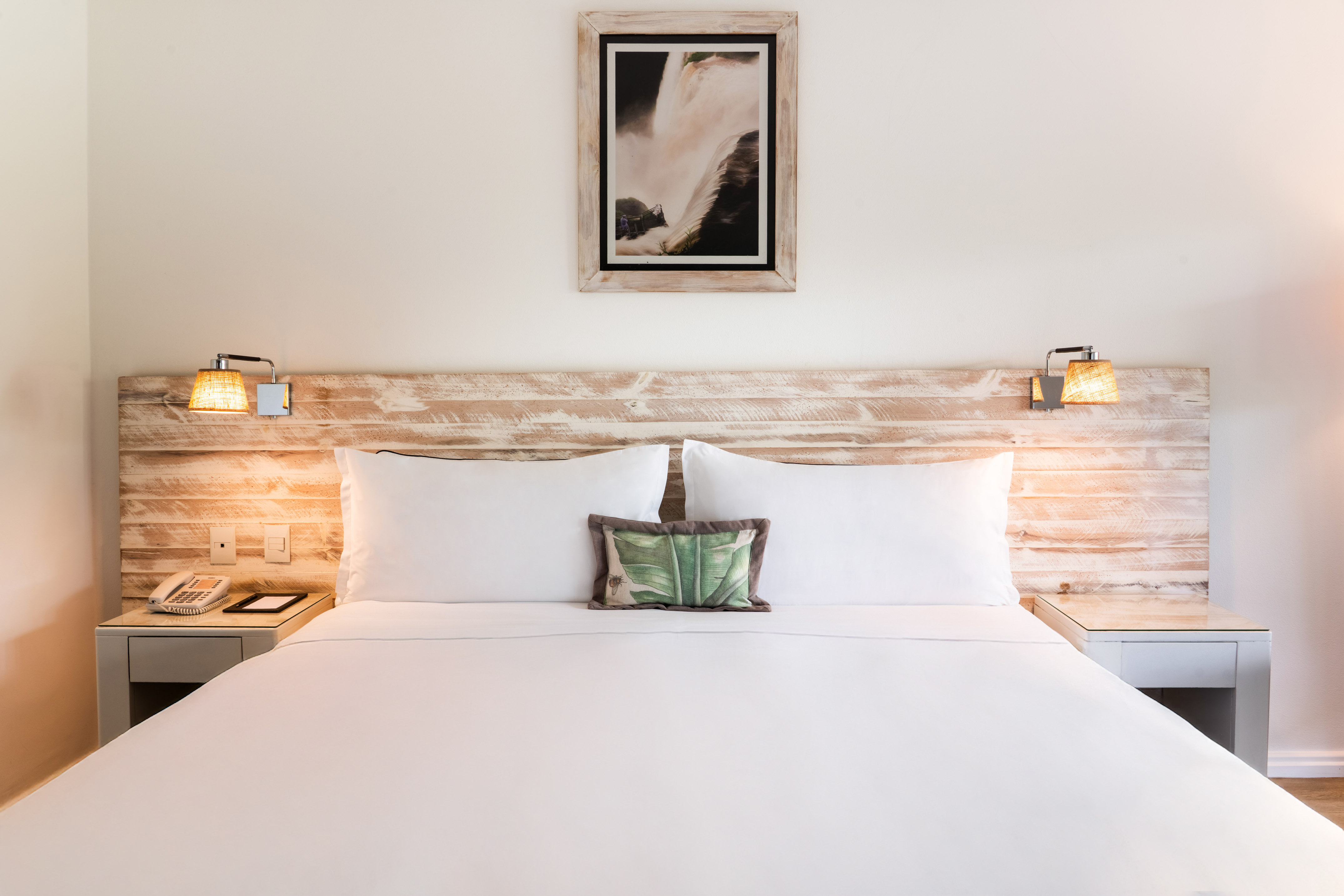Hotel room with white bed, rustic wooden headboard, bedside lamps, waterfall art. - Deluxe Room King Size Bed – Jungle View - Gran Meliá Iguazú, Εθνικό Πάρκο Iguazú