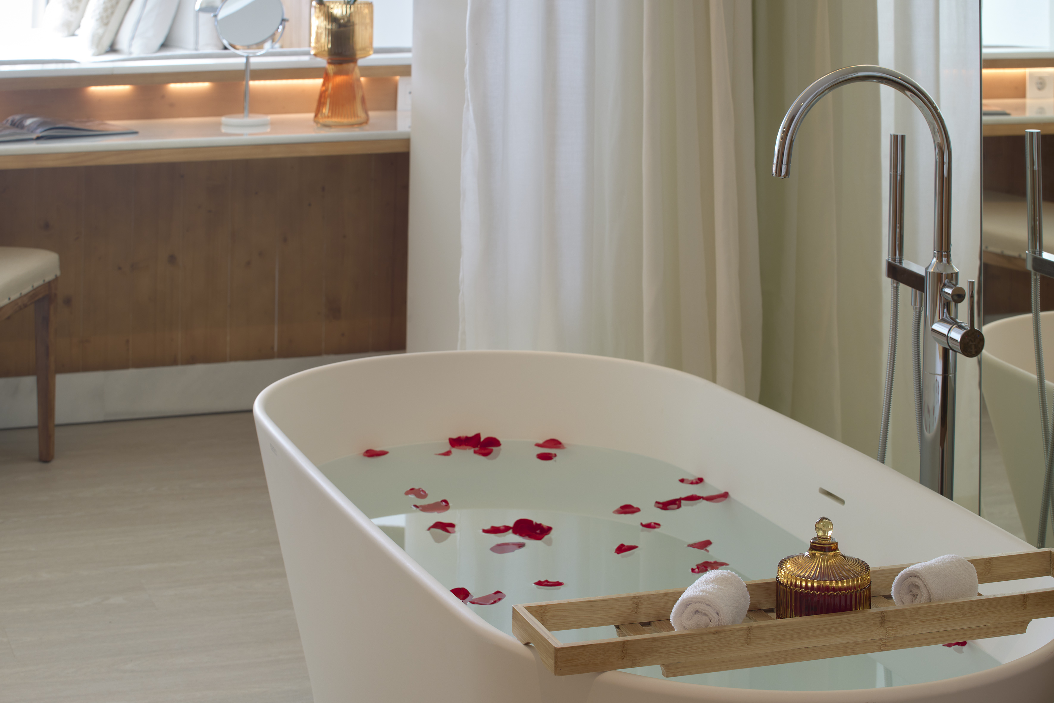 White freestanding bathtub with rose petals, luxury spa bathroom.