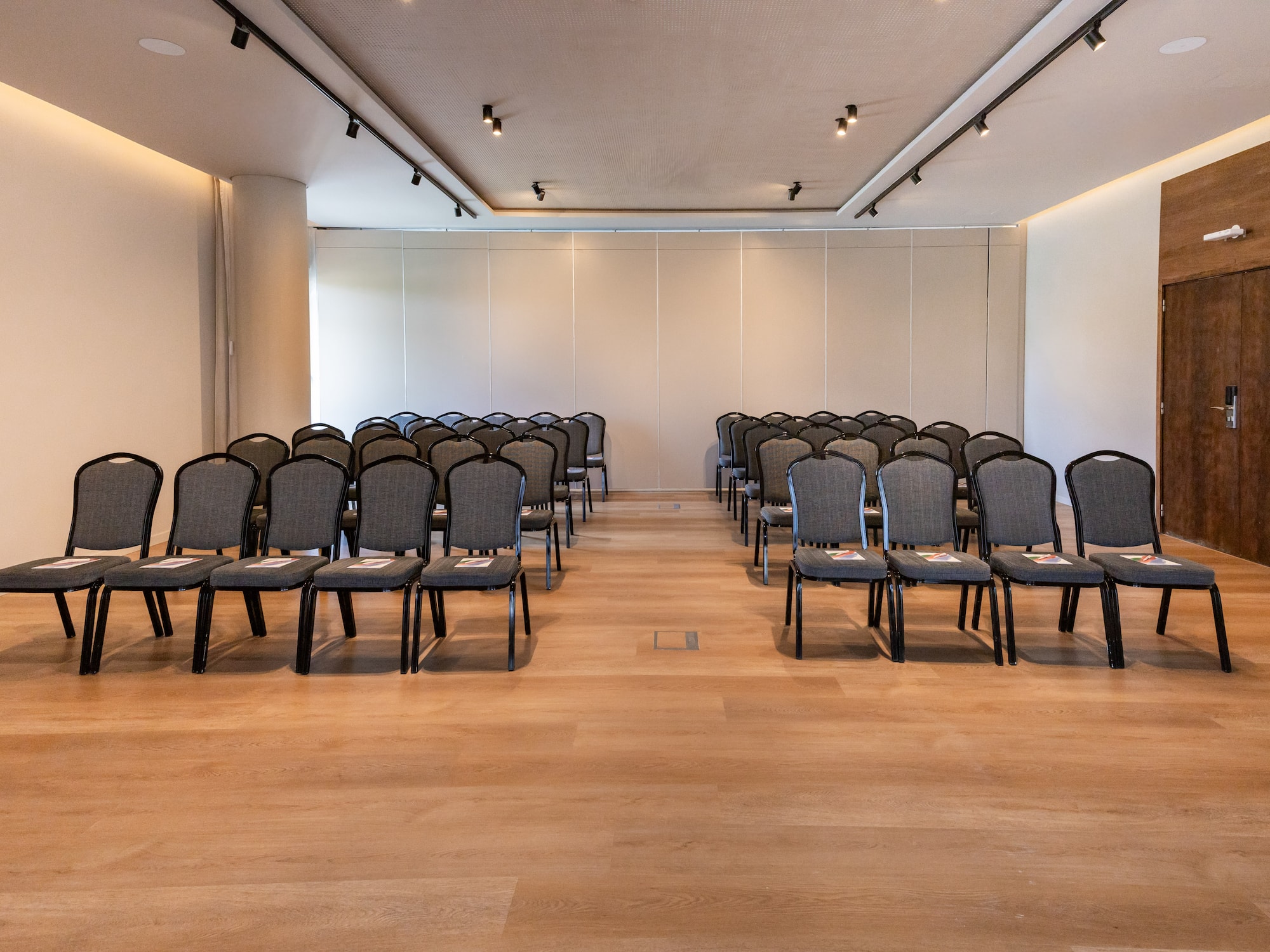 Empty modern conference hall with rows of grey chairs on a hardwood floor.