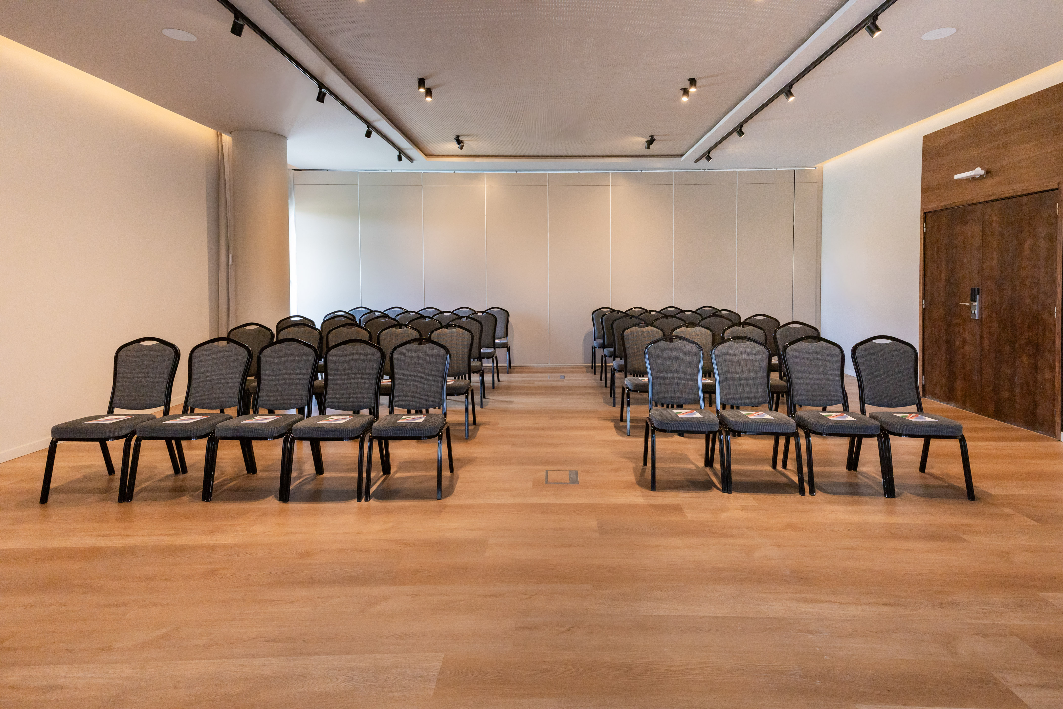 Empty modern conference hall with rows of grey chairs on a hardwood floor.