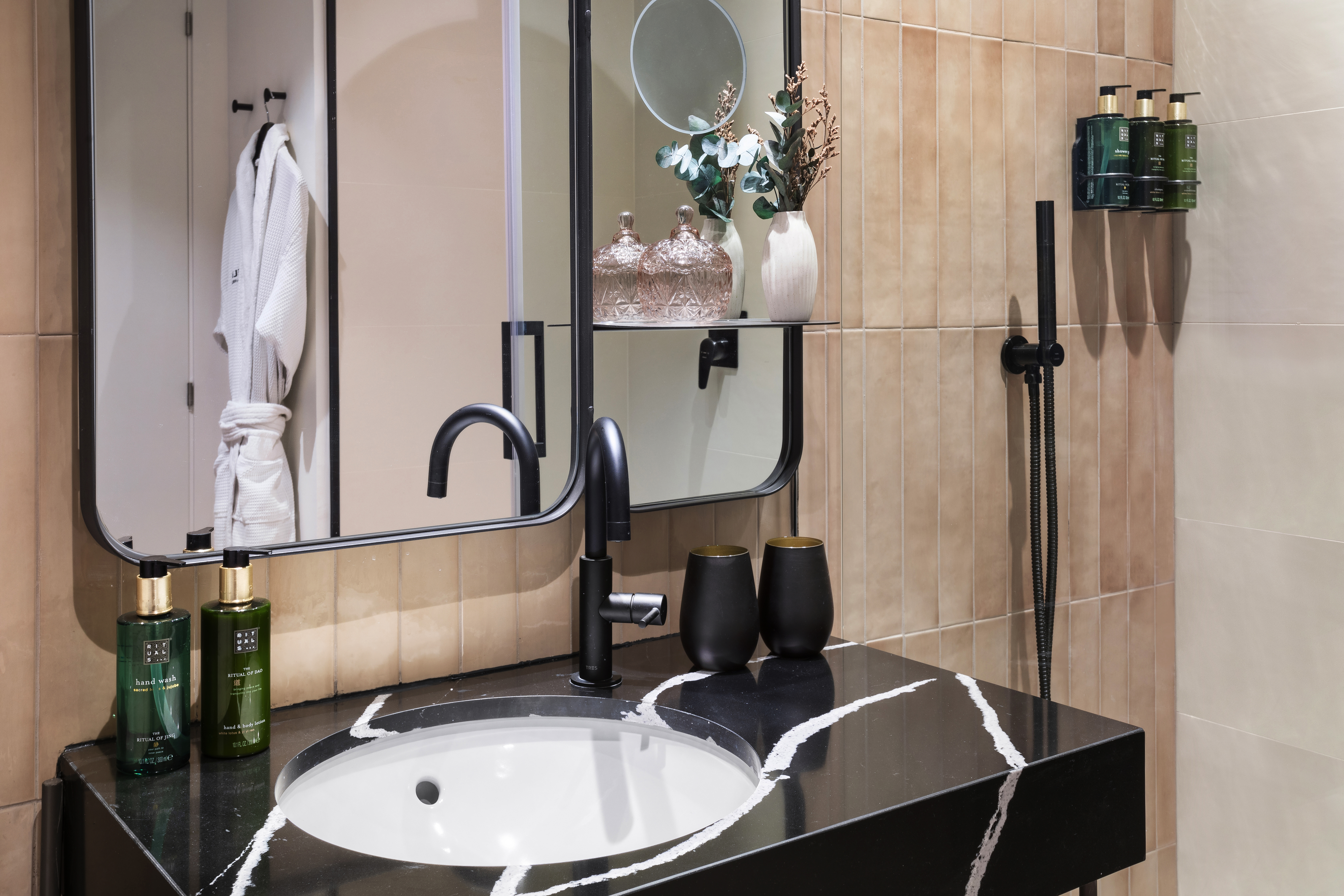 Modern bathroom vanity with black marble, white sink, black faucet, and Rituals products.
