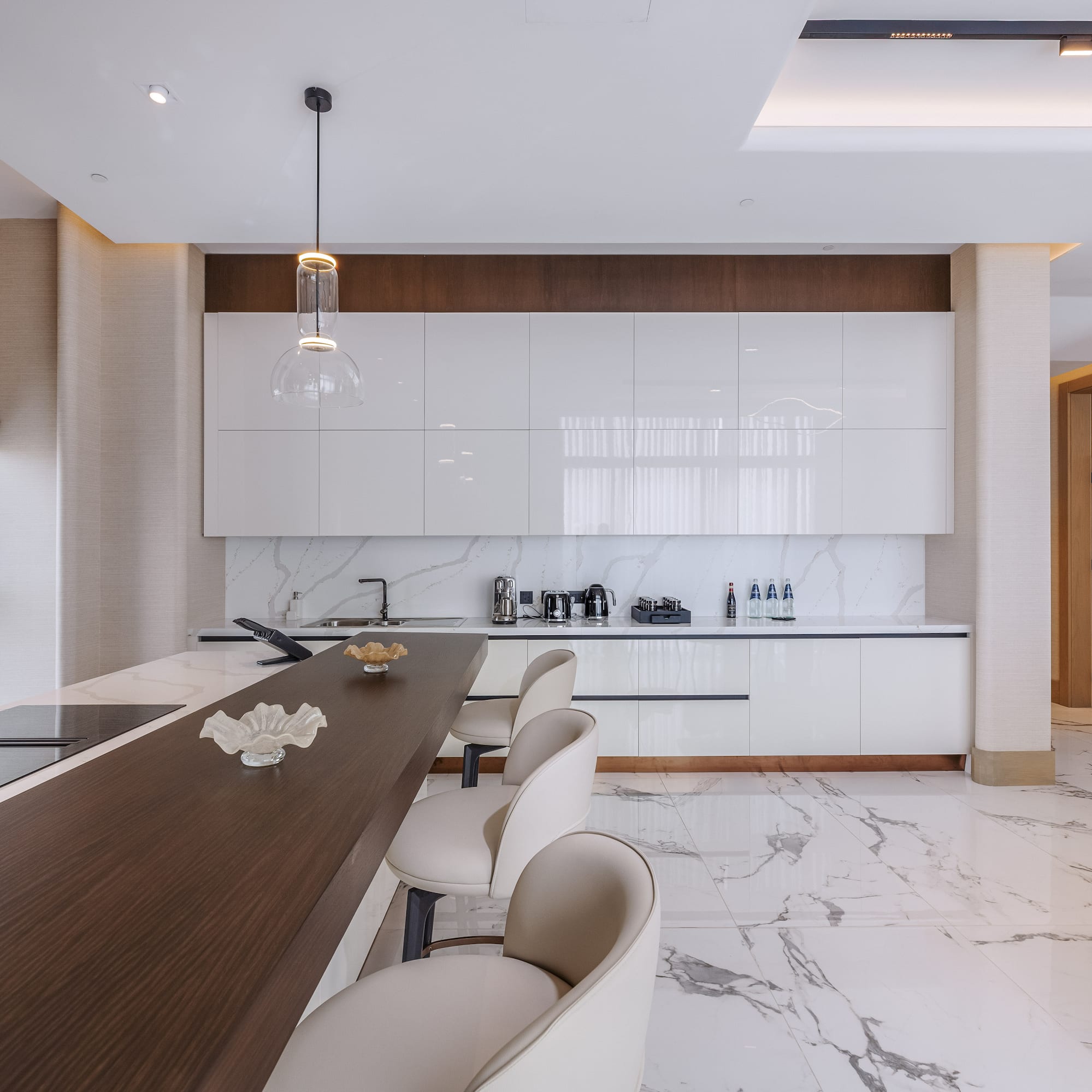 Modern kitchen featuring white cabinets, marble floor, dark island, and bar stools.