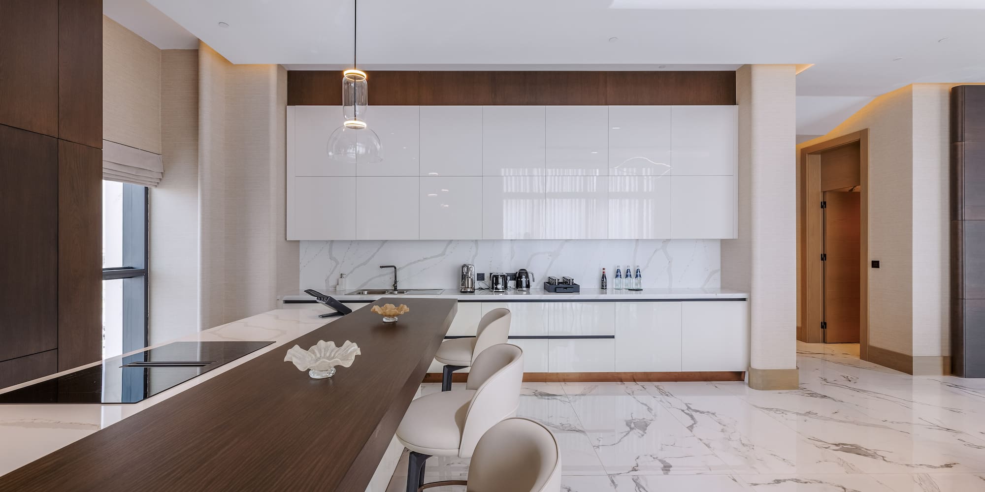Modern kitchen featuring white cabinets, marble floor, dark island, and bar stools.