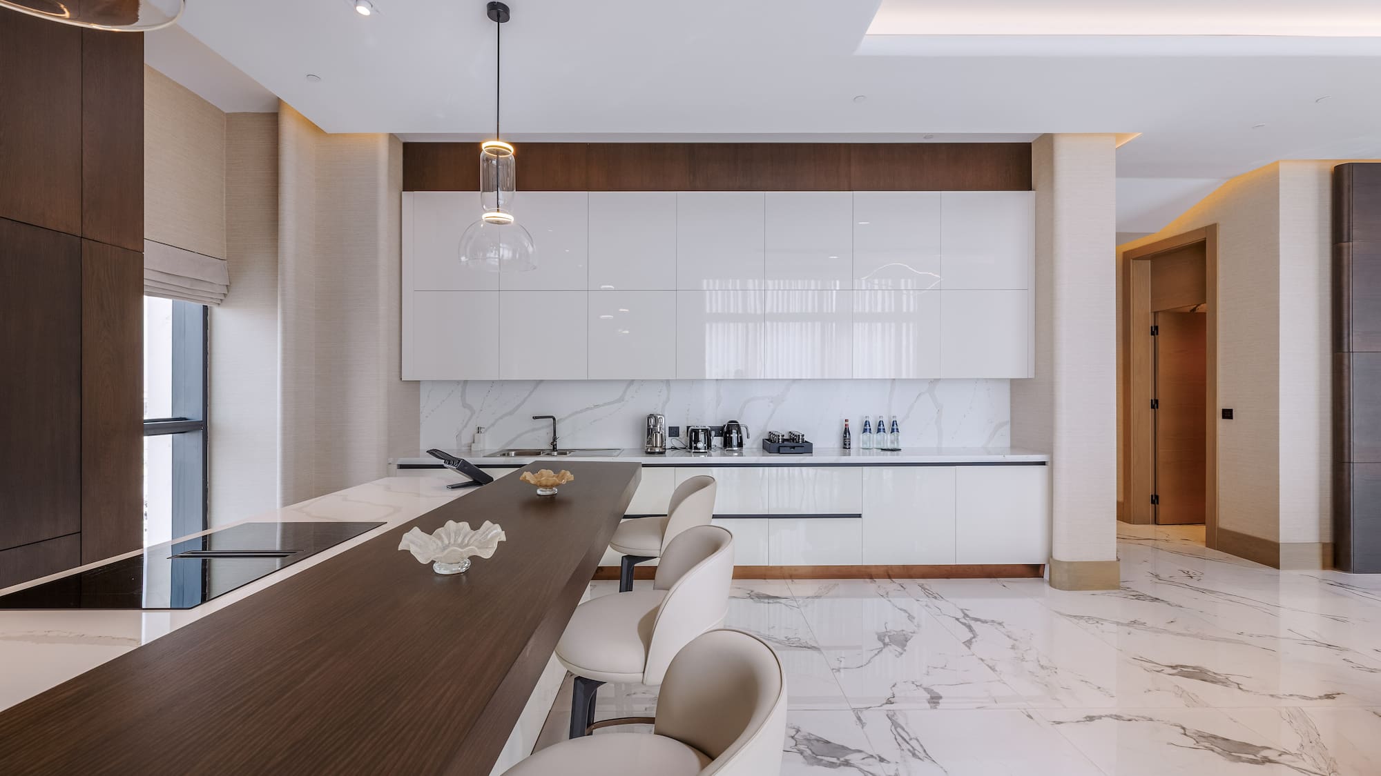 Modern kitchen featuring white cabinets, marble floor, dark island, and bar stools.