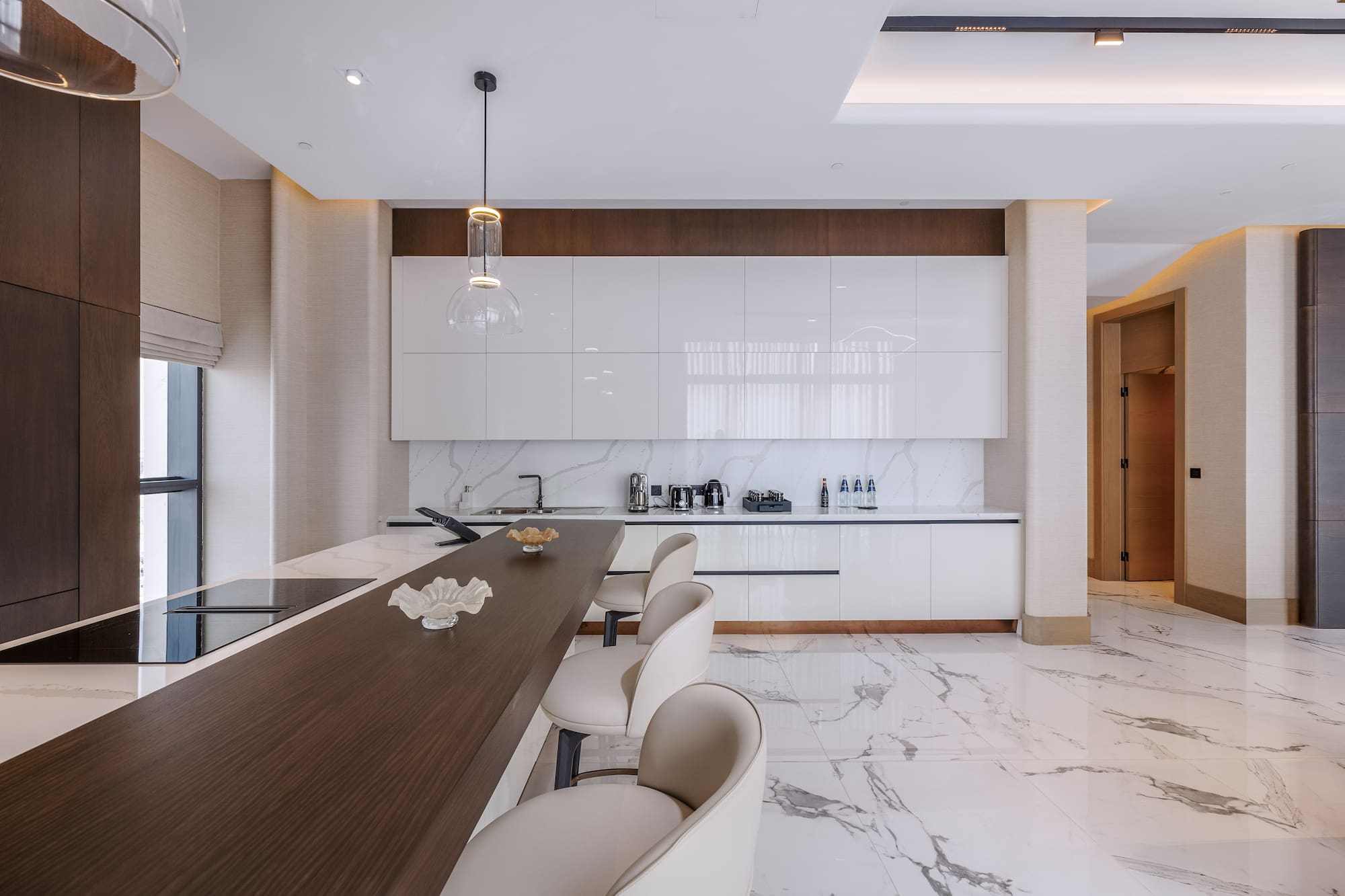 Modern kitchen featuring white cabinets, marble floor, dark island, and bar stools.