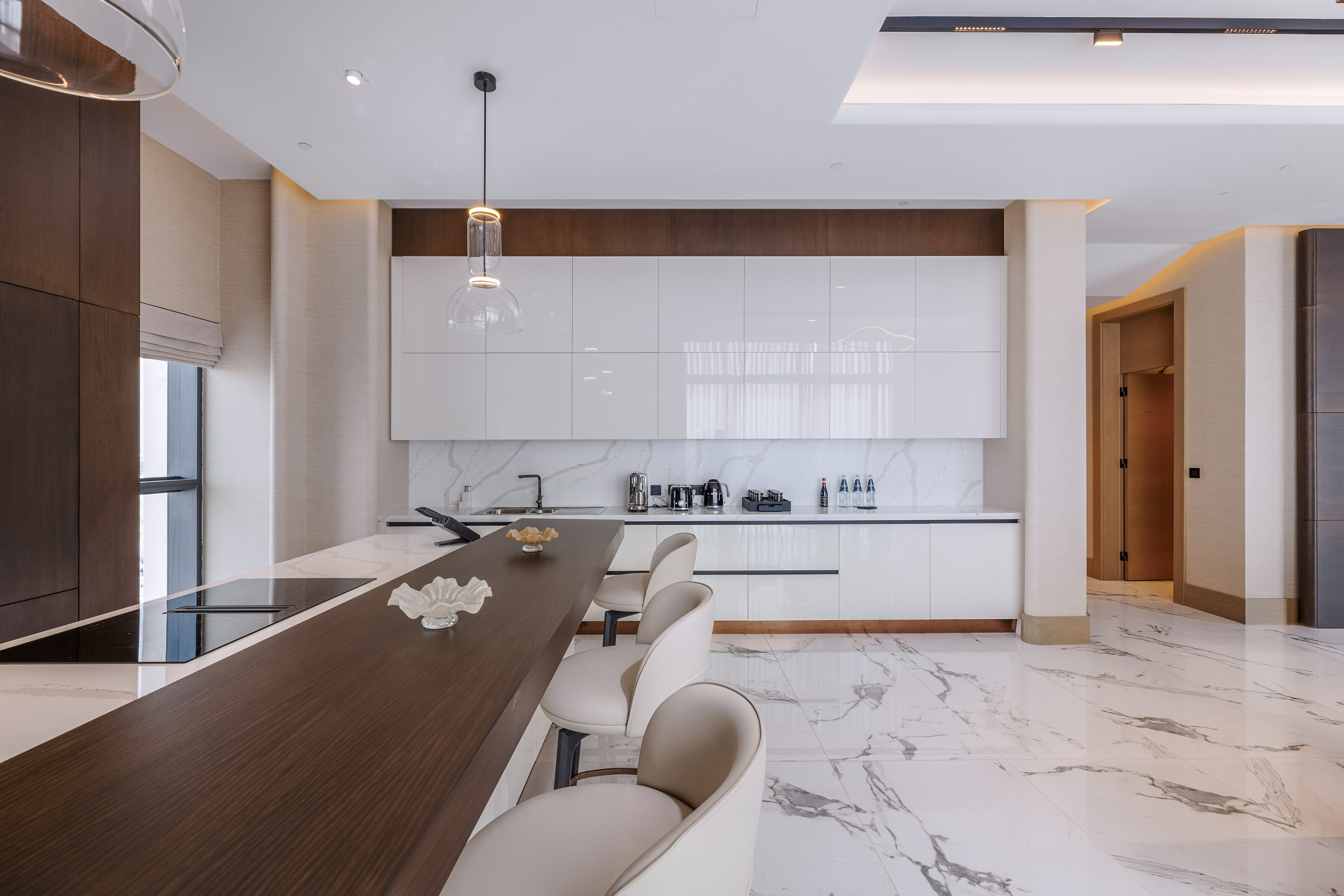 Modern kitchen featuring white cabinets, marble floor, dark island, and bar stools.
