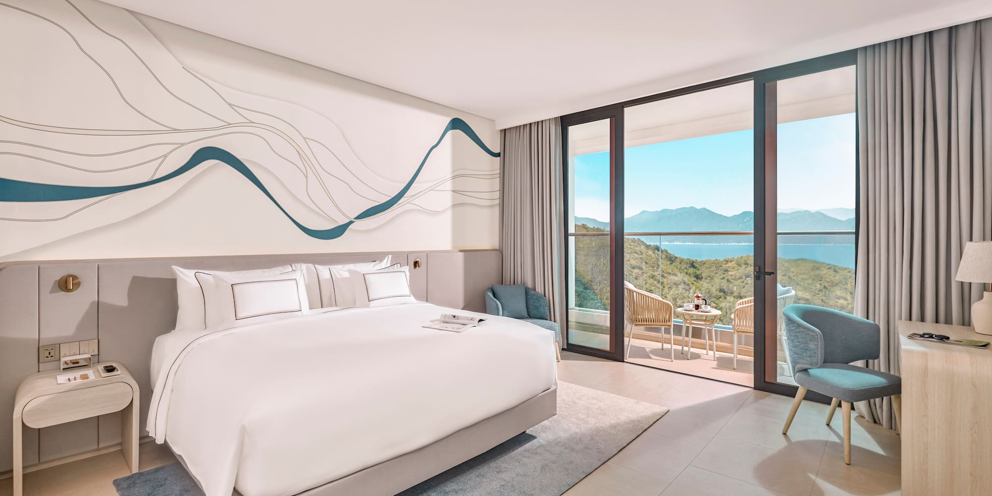Modern hotel bedroom with ocean view balcony, white bed, blue decor.