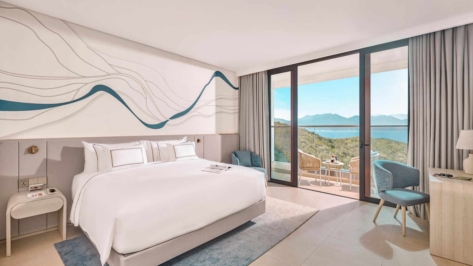 Modern hotel bedroom with ocean view balcony, white bed, blue decor.