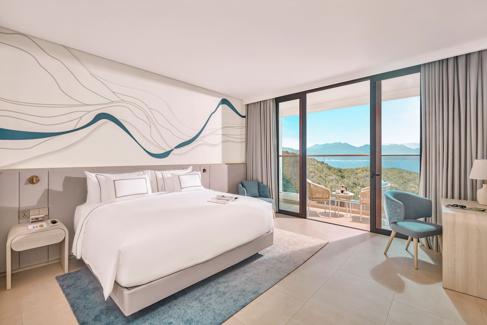 Modern hotel bedroom with ocean view balcony, white bed, blue decor.