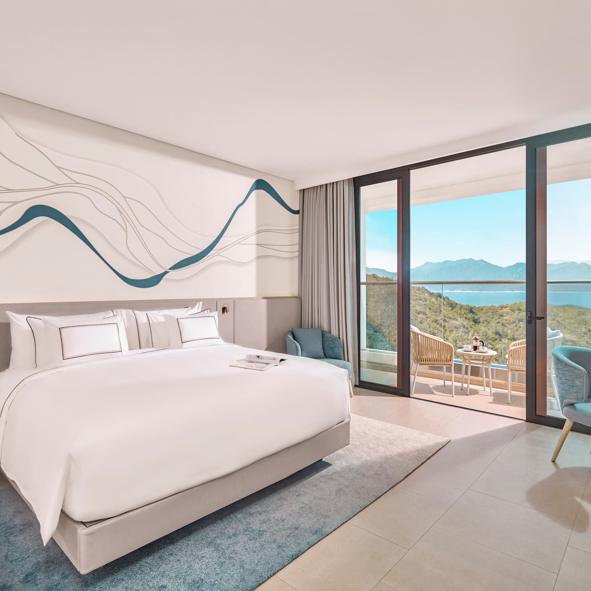 Modern hotel bedroom with ocean view balcony, white bed, blue decor.