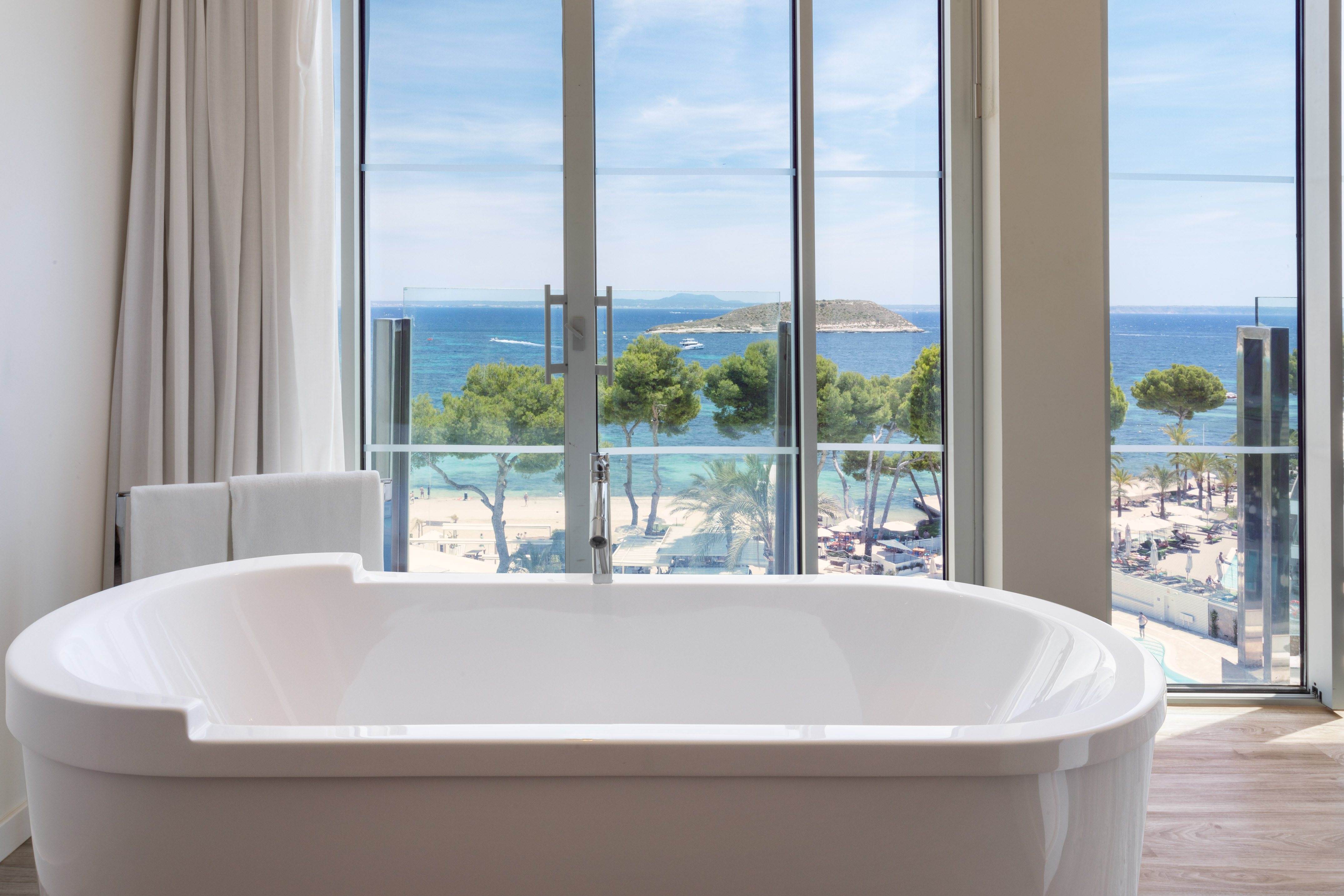 White bathtub, ocean view, sandy beach, and island from hotel windows.