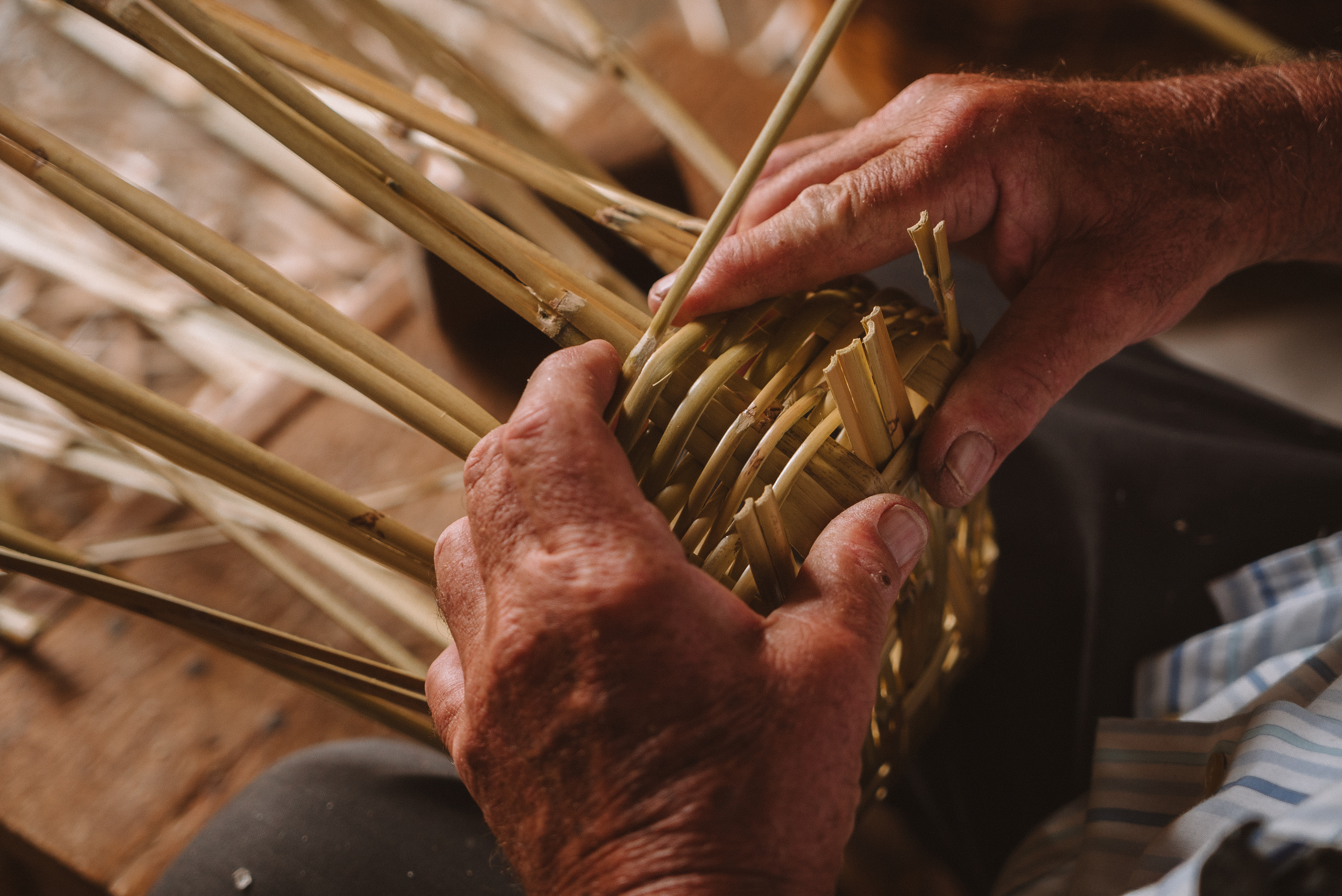 Artisan's hands weaving a natural rattan basket.