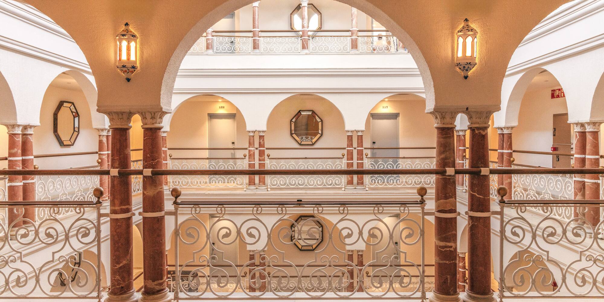 Luxury hotel interior with arched hallways, marble columns, and intricate railings.