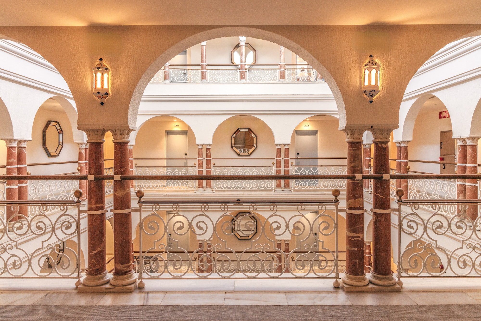 Luxury hotel interior with arched hallways, marble columns, and intricate railings.