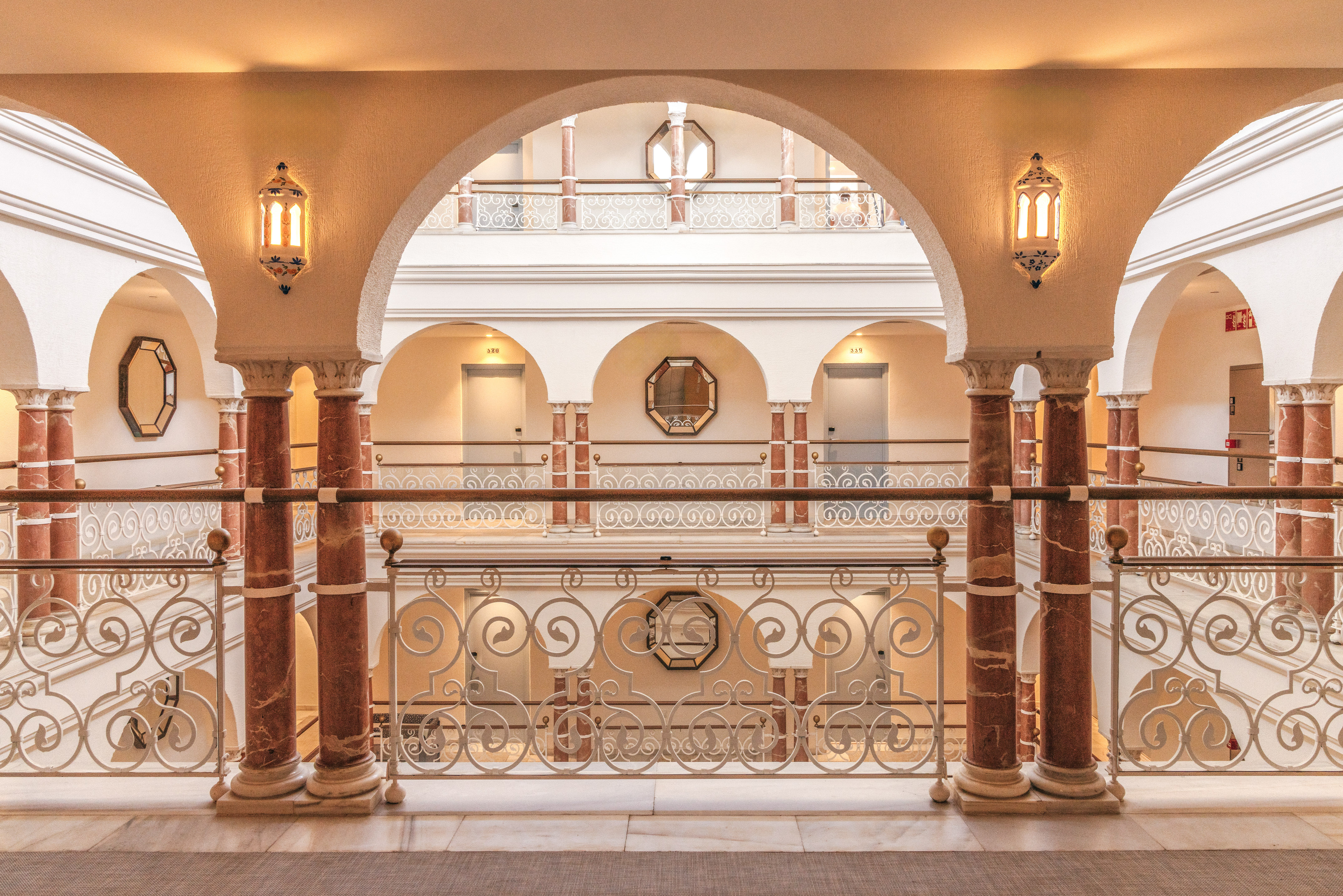 Luxury hotel interior with arched hallways, marble columns, and intricate railings.