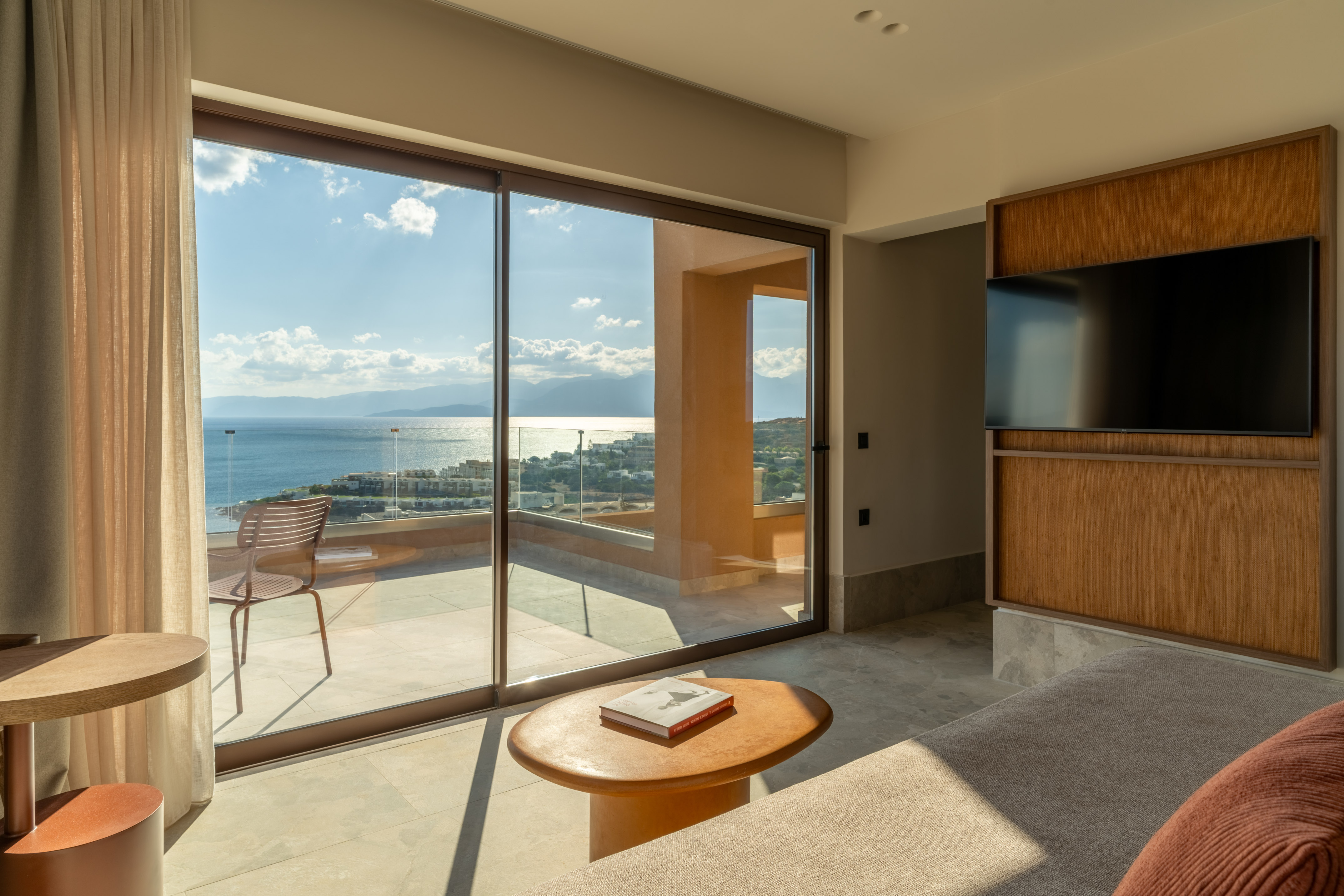 Modern hotel room with sea view balcony, sofa, TV, and coffee table.