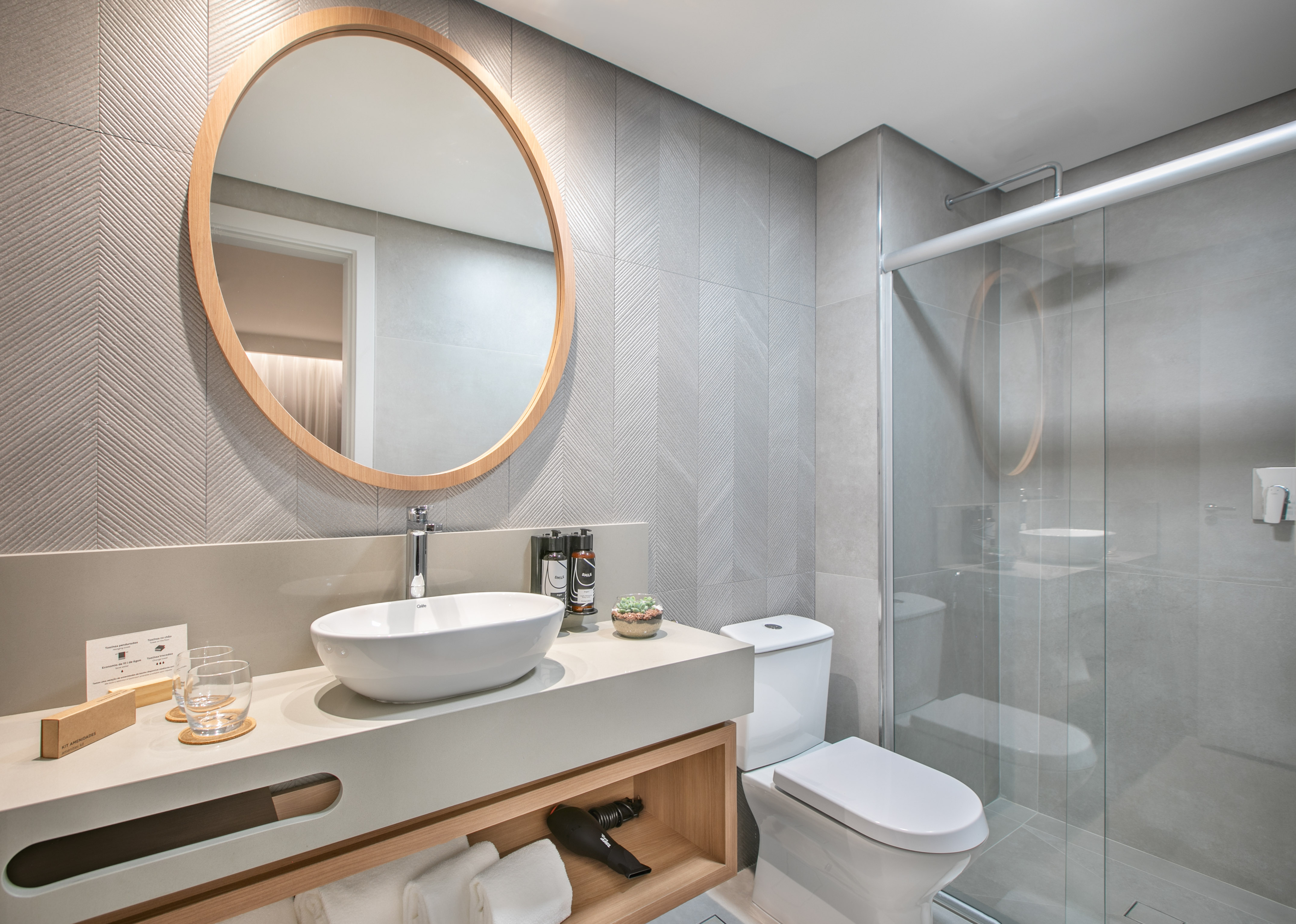 Modern bathroom with gray chevron tiles, wood mirror, white sink, glass shower.
