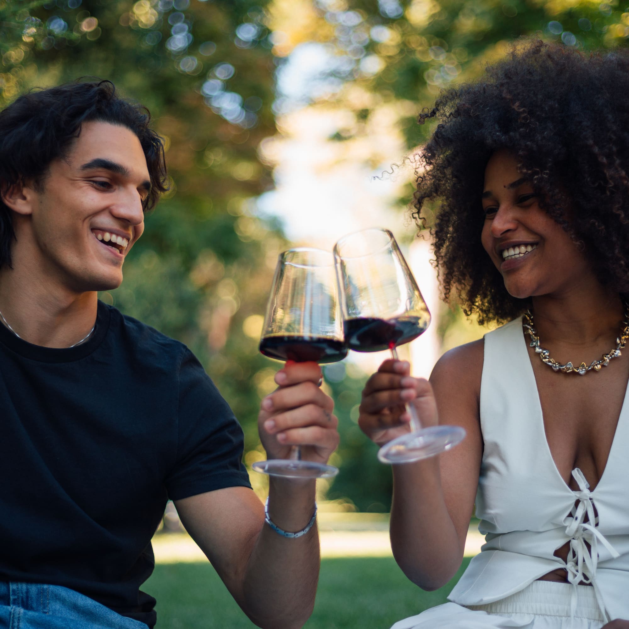 a man and woman sitting on grass and holding wine glasses