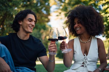 a man and woman sitting on grass and holding wine glasses