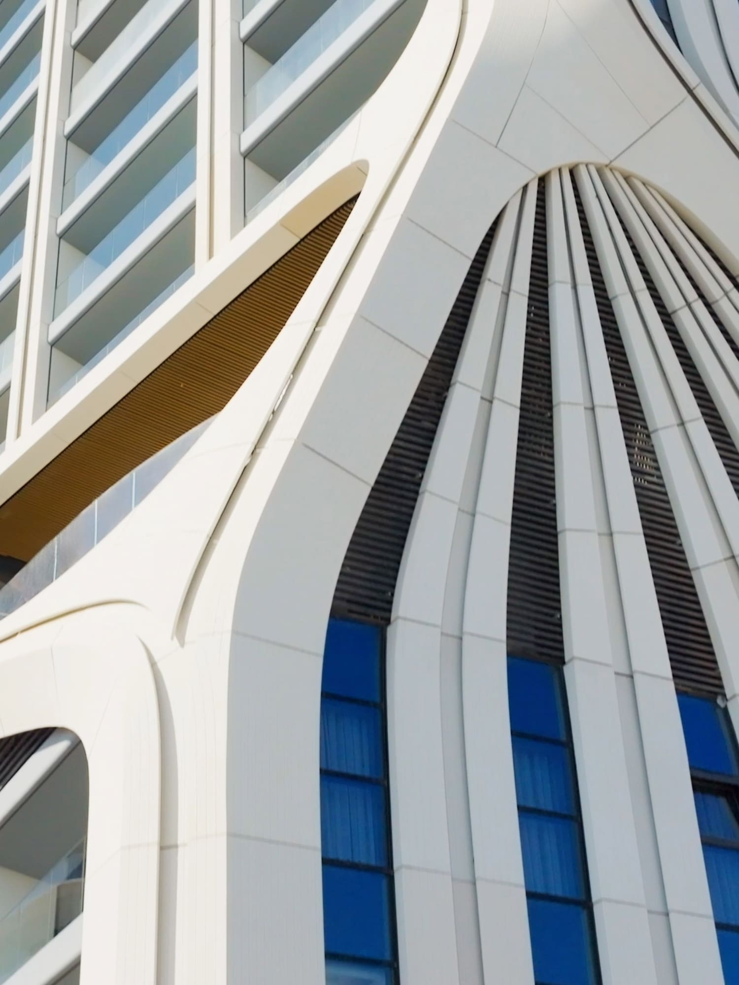 Modern white building facade with undulating curves and blue windows.
