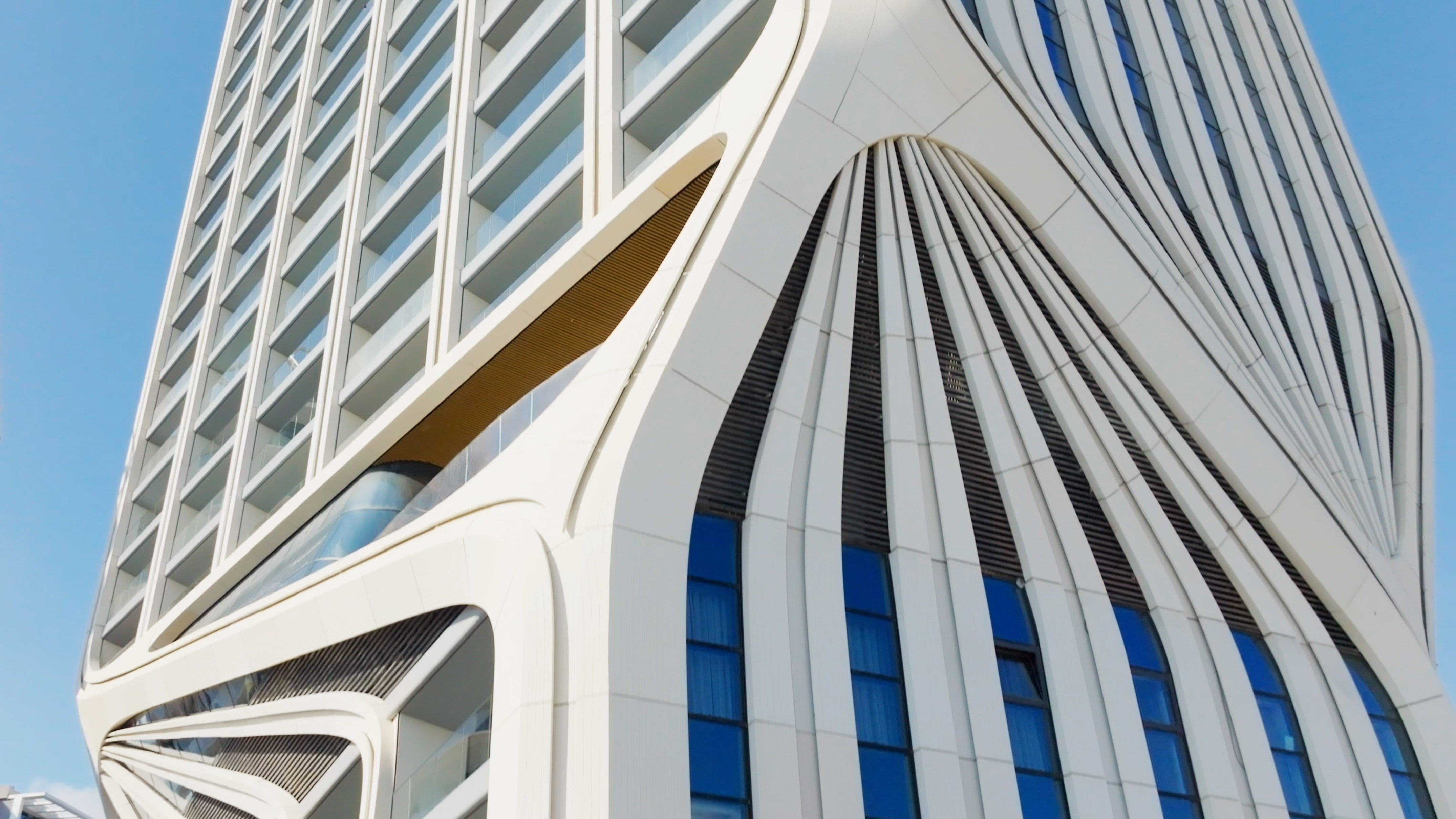 Modern white building facade with undulating curves and blue windows.