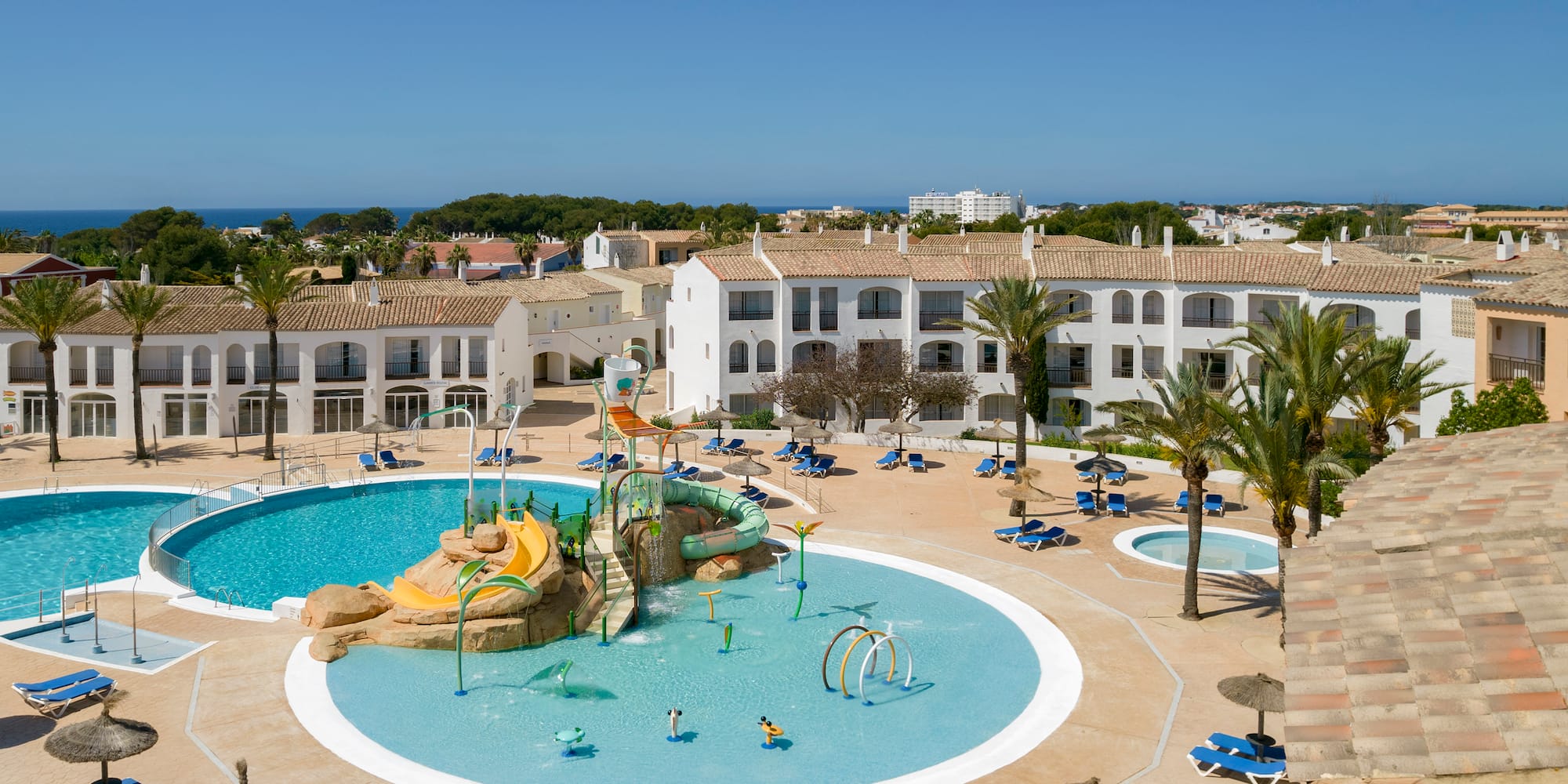 Coastal resort: large pools, kids' water park with slides, and hotel buildings.