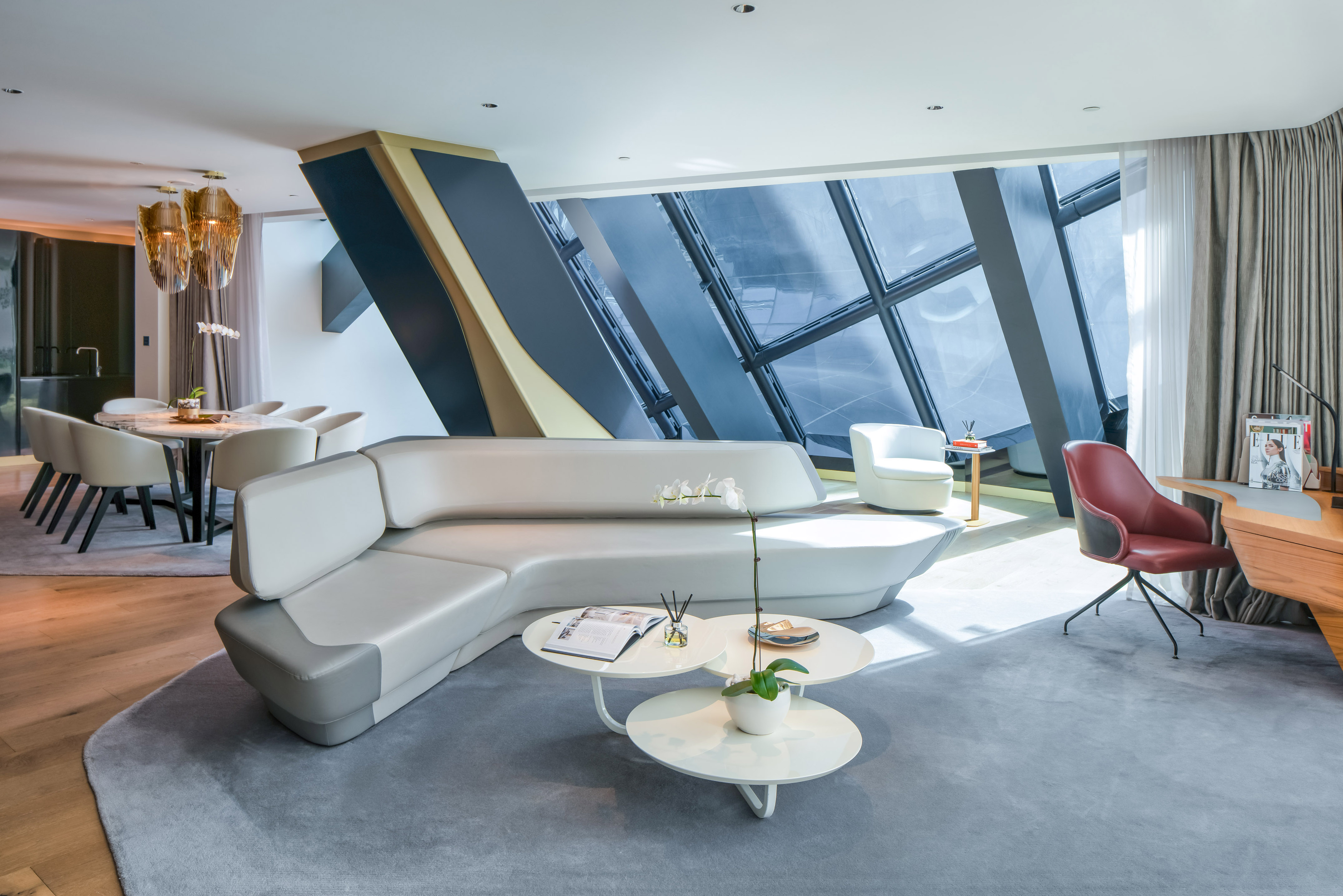 Chic modern living room: grey curved sectional, dining, geometric windows.