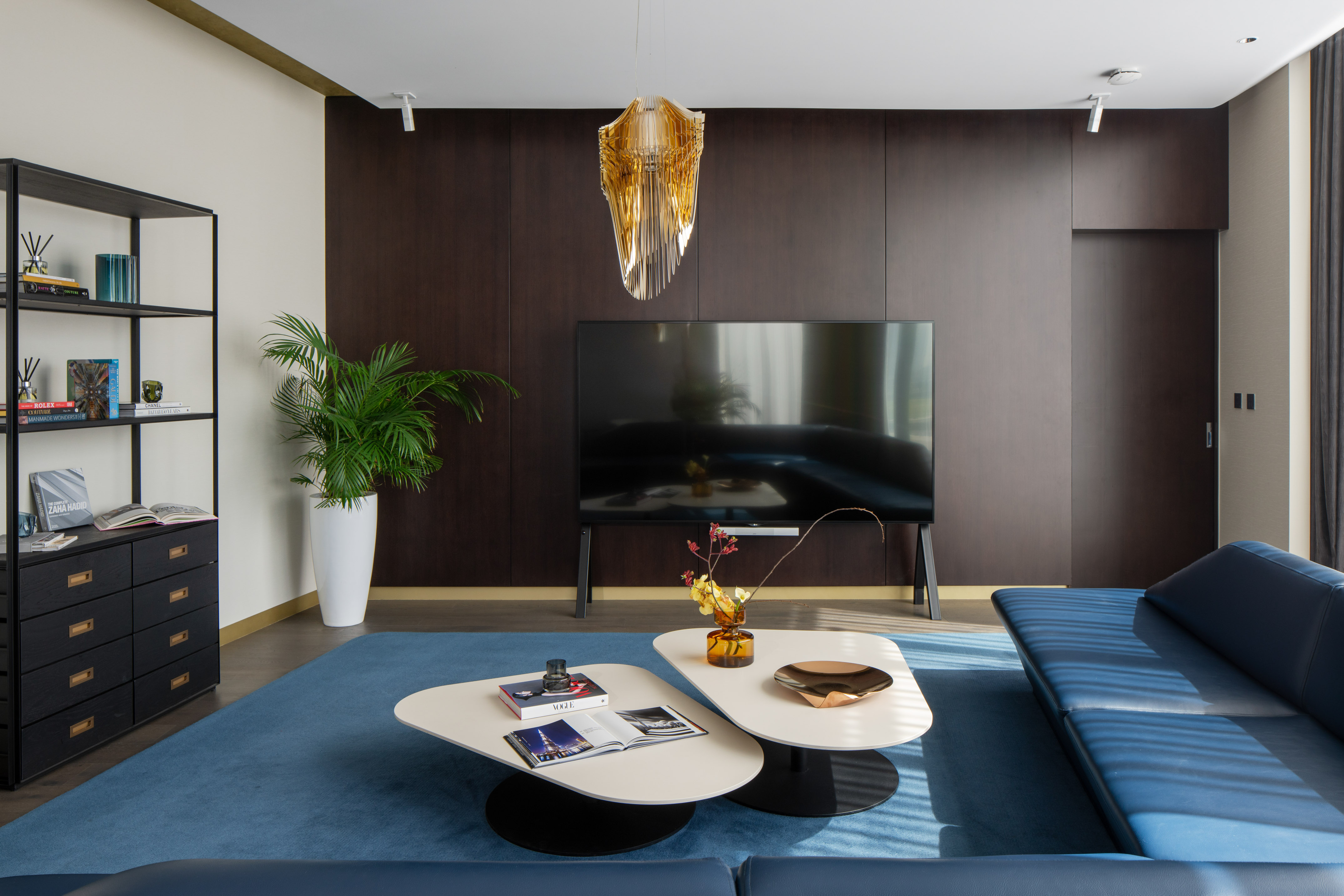 Modern living room with blue sofa, dark wood wall, and unique golden chandelier.