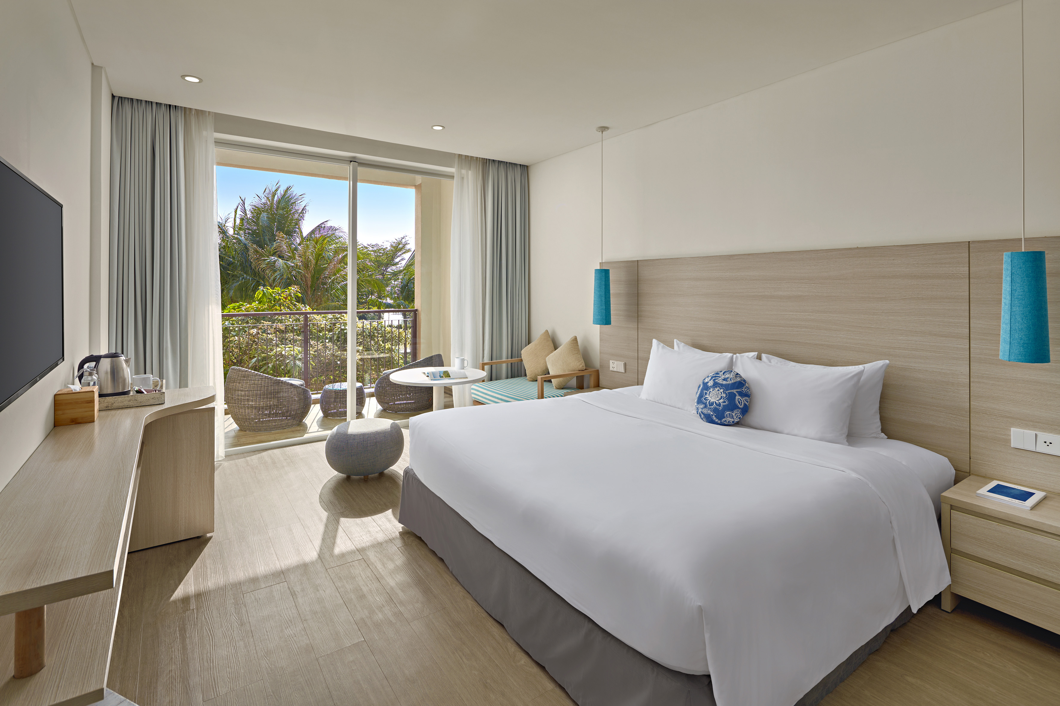 Modern hotel room with king bed, balcony, and tropical resort view.