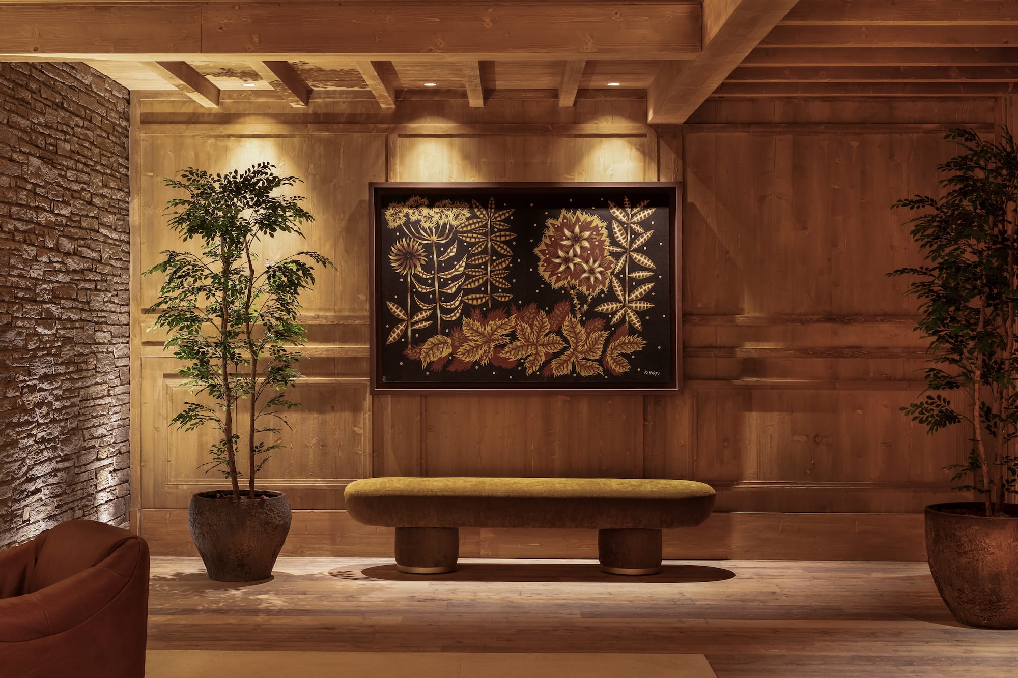 Chalet interior with floral painting, olive bench, wood walls, and plants.