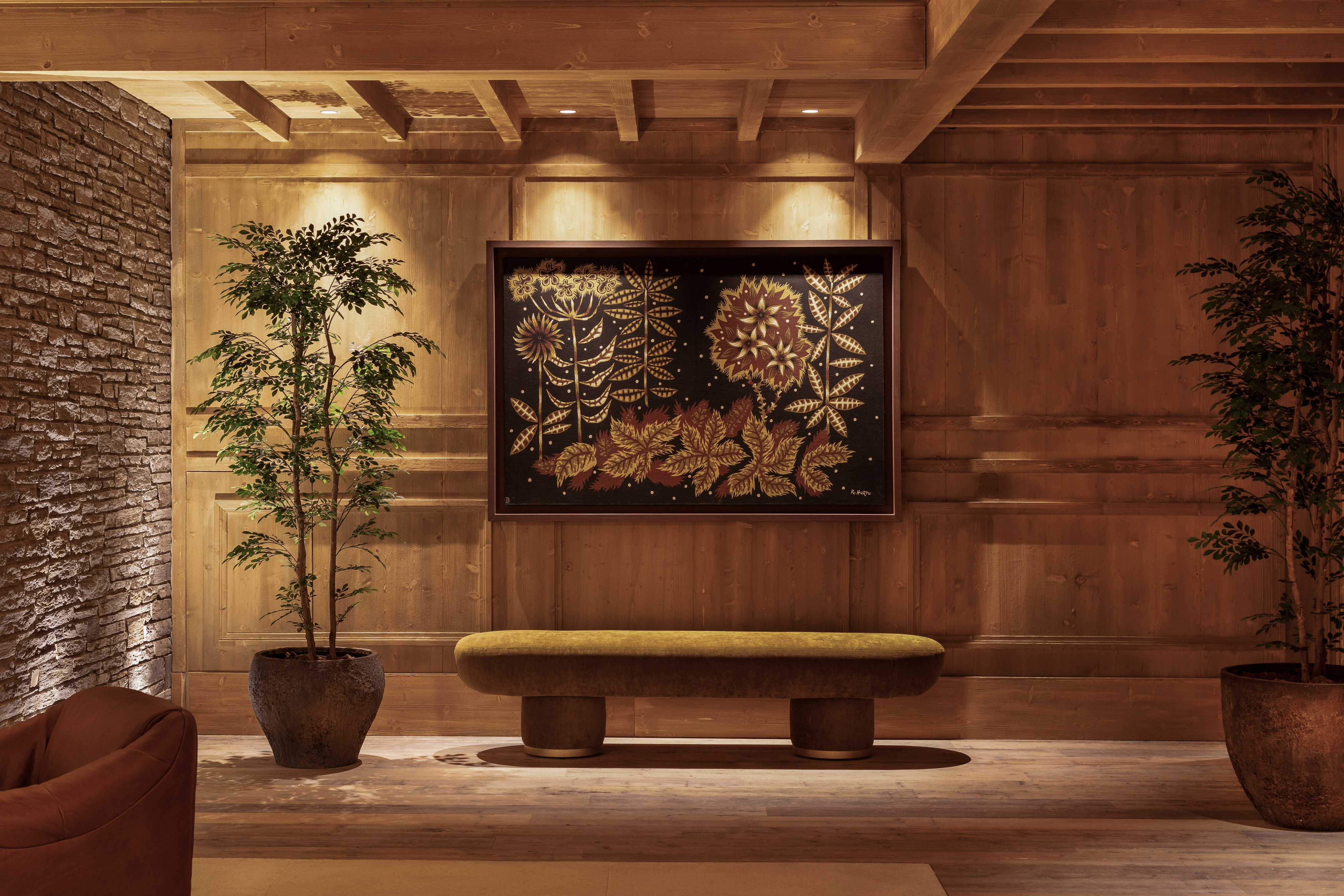 Chalet interior with floral painting, olive bench, wood walls, and plants.