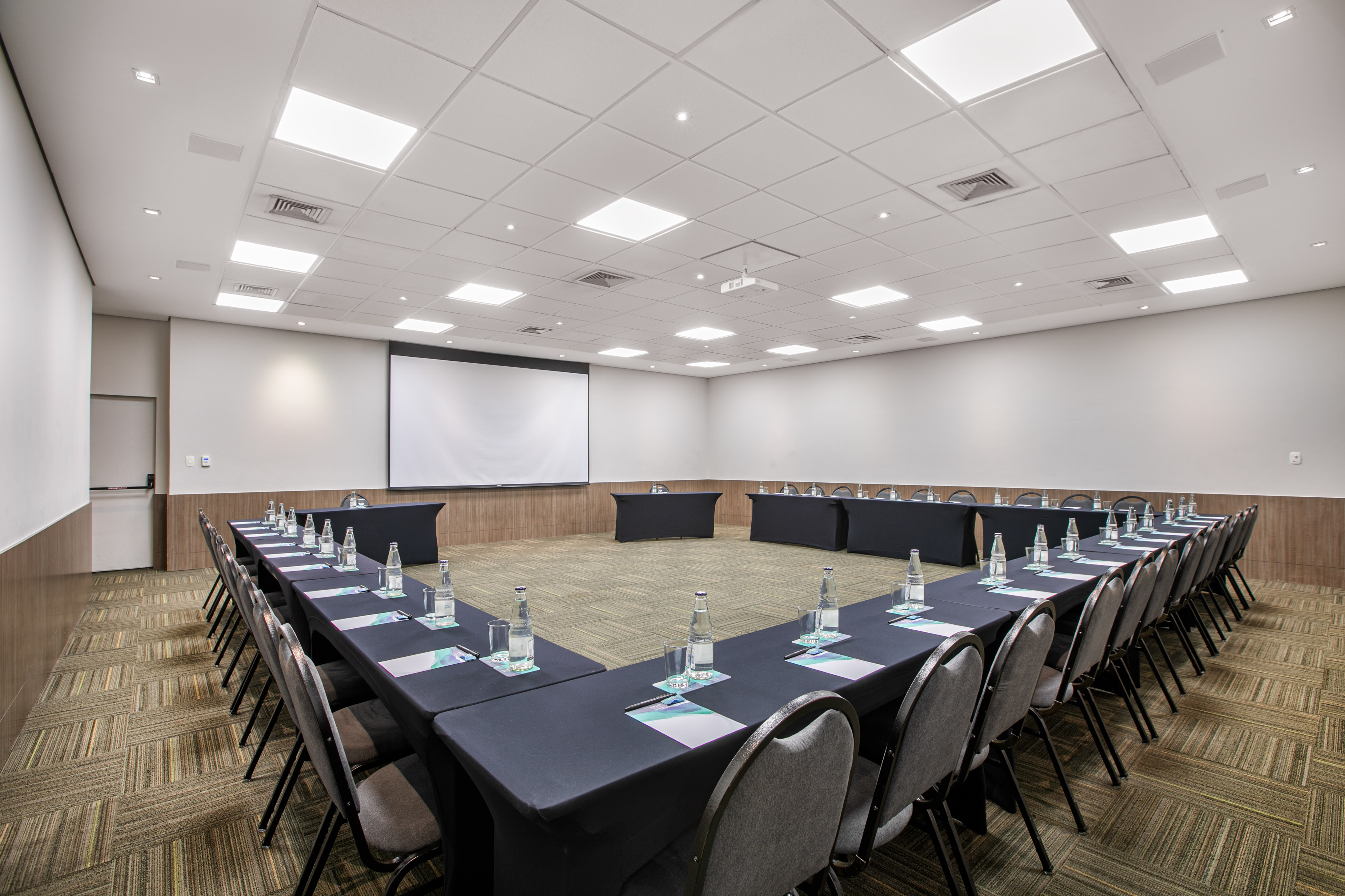 Professional conference room with U-shaped tables, screen, and projector.