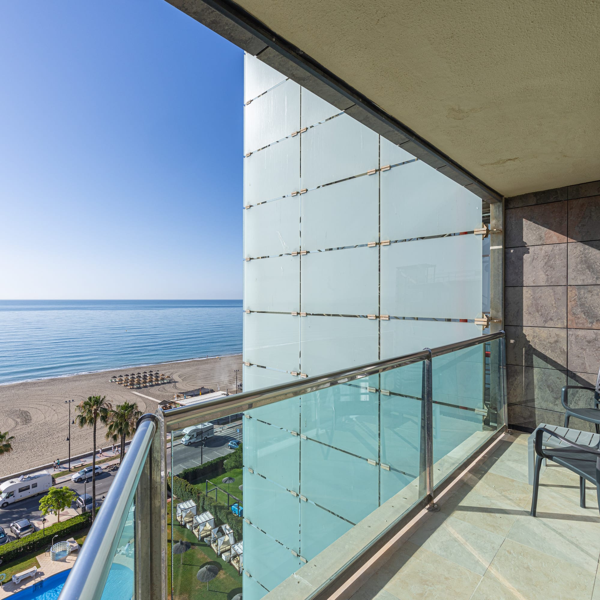 Sunny hotel balcony with ocean view, sandy beach, and palm trees.