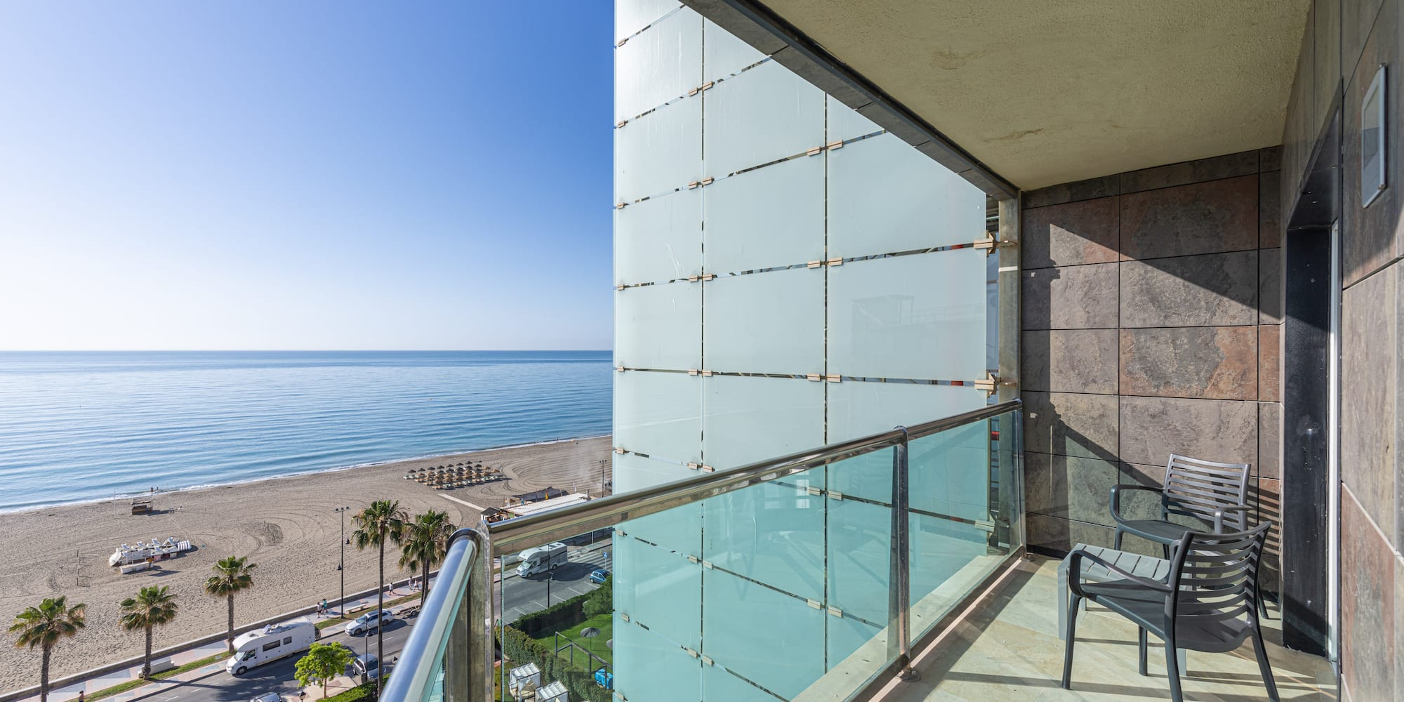Sunny hotel balcony with ocean view, sandy beach, and palm trees.