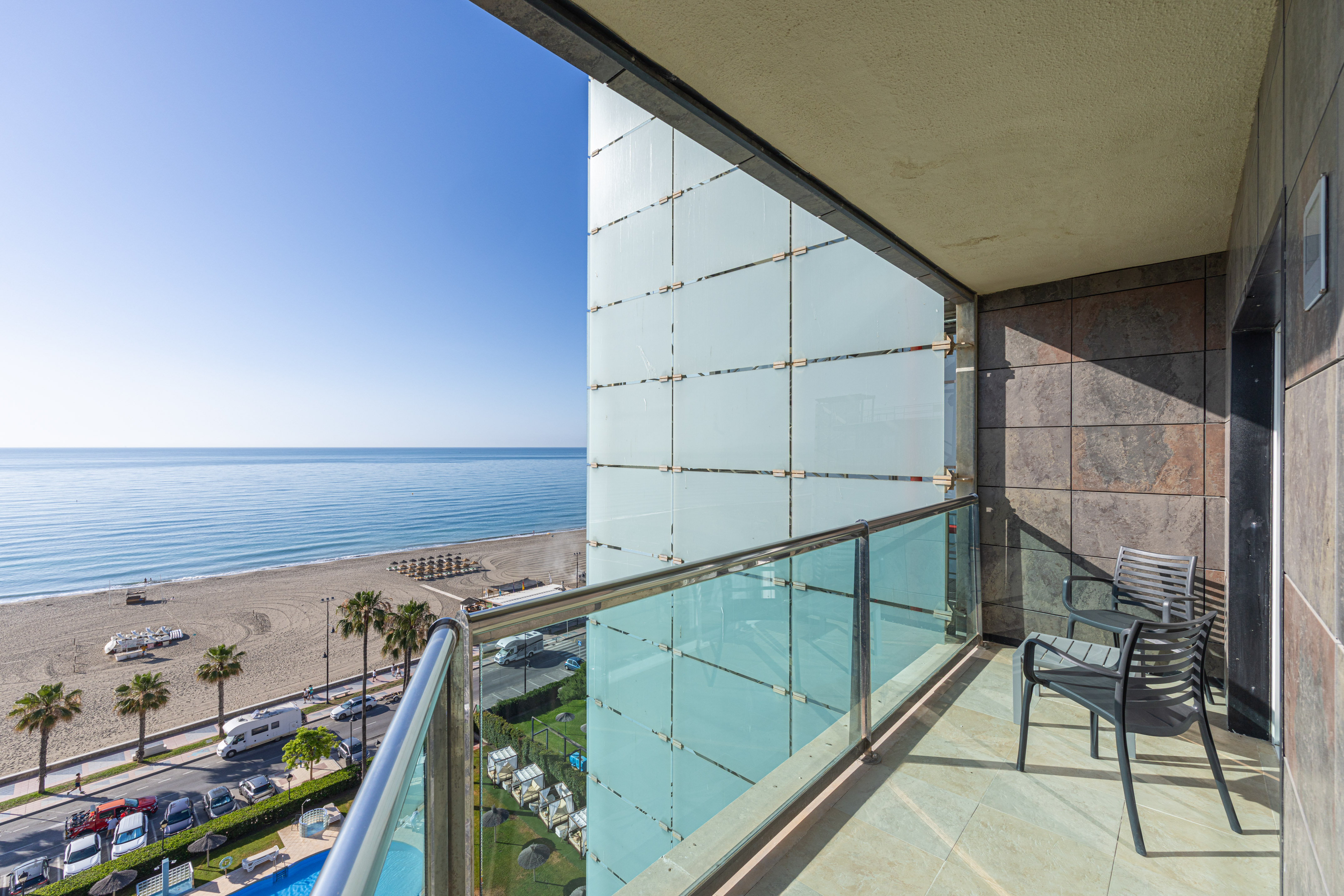 Resort balcony with oceanfront view, sandy beach, palm trees, and frosted glass.