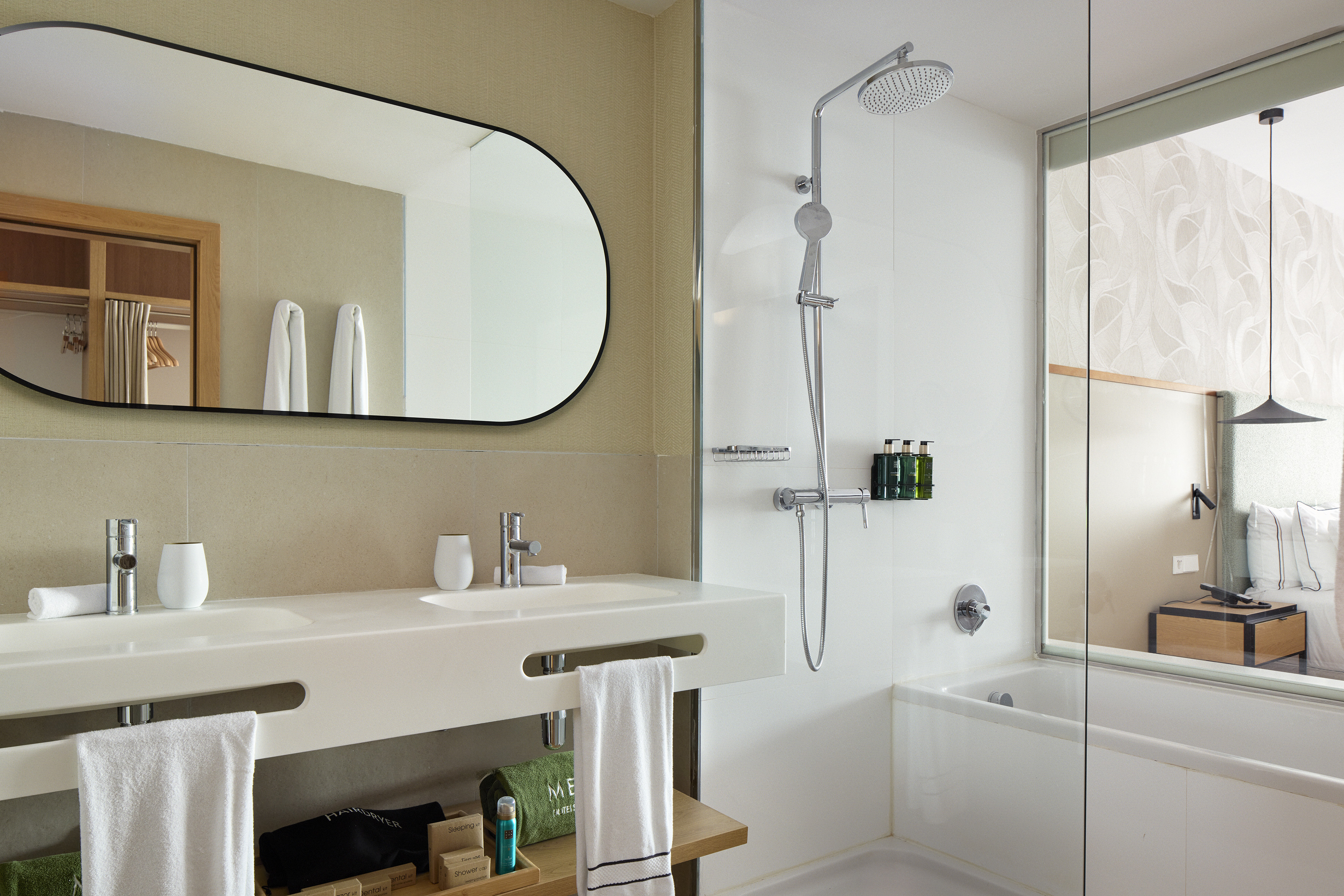 Modern hotel bathroom with double vanity, shower, bathtub, oval mirror.