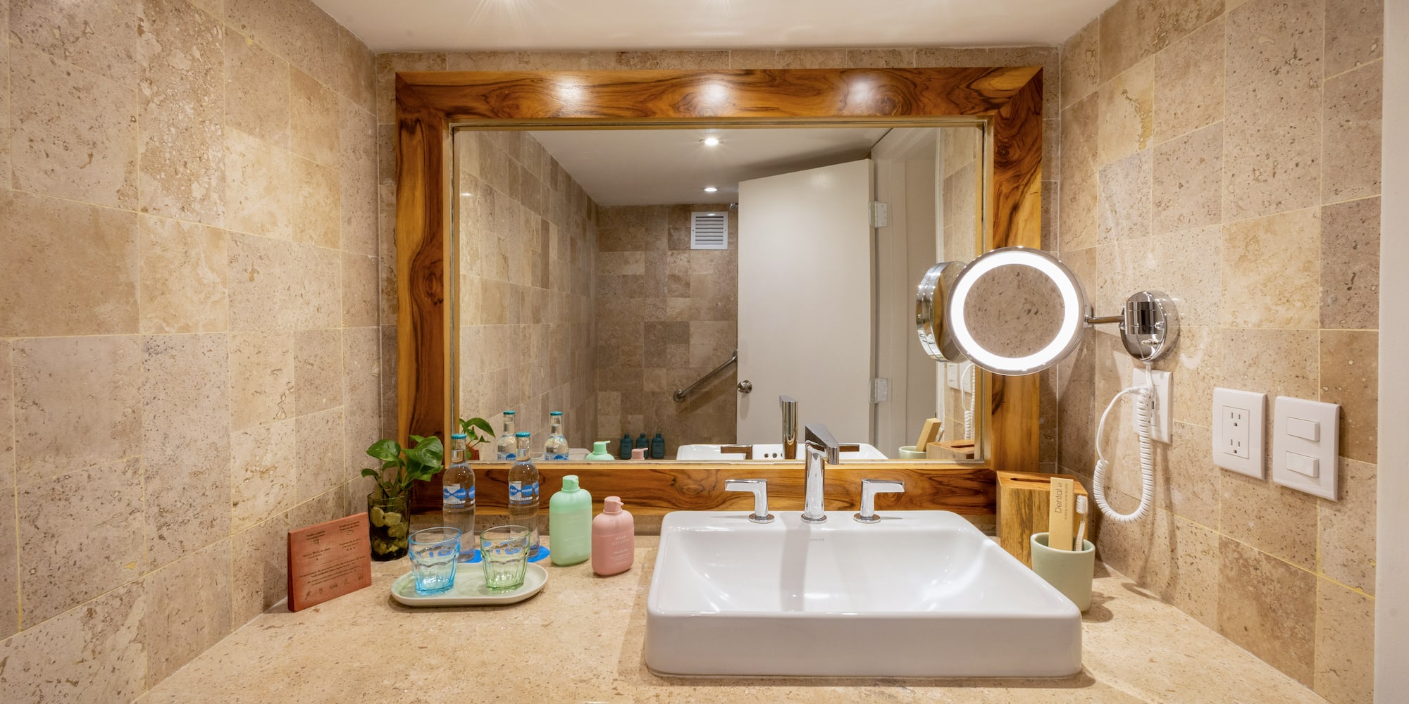 Luxury hotel bathroom with travertine vanity, sleek sink, and illuminated mirror.