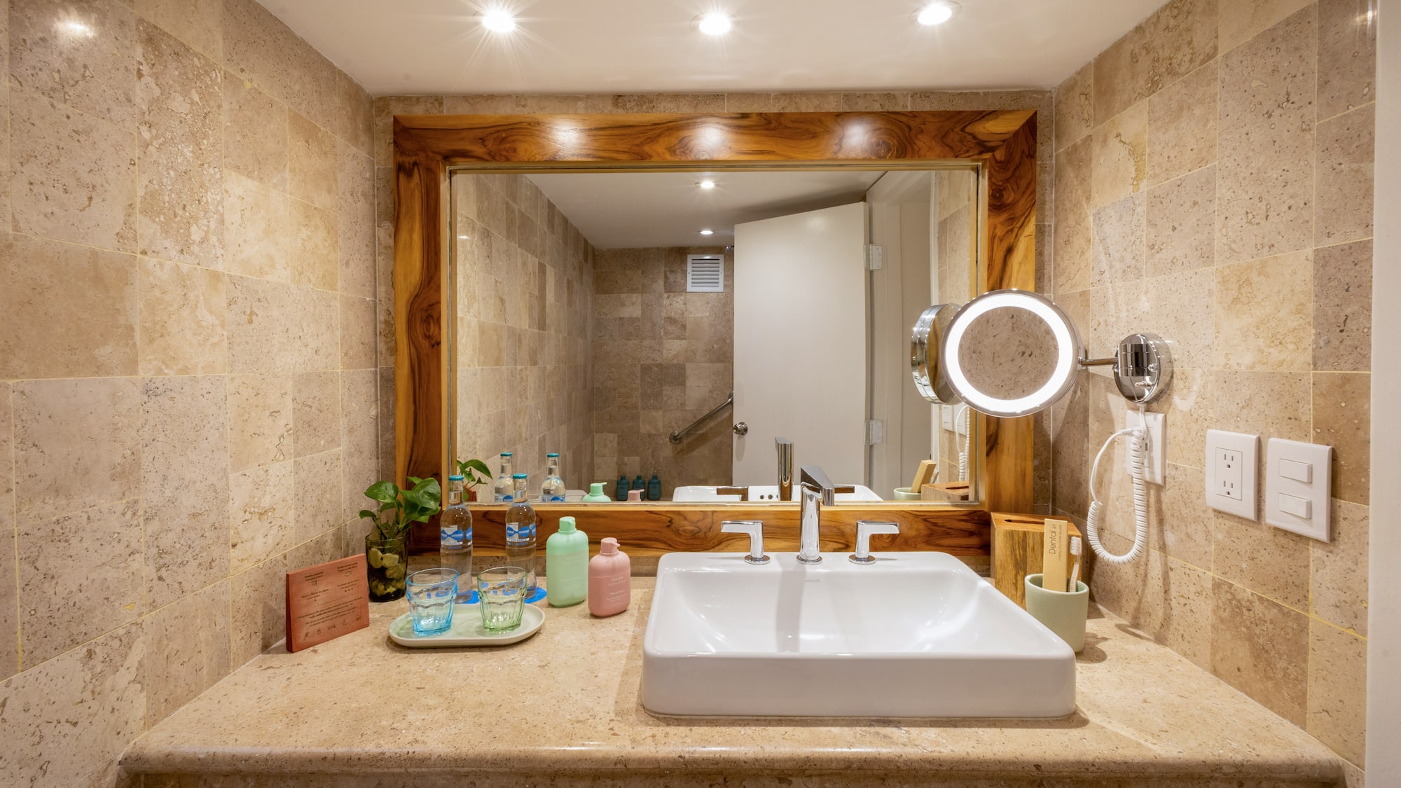 Luxury hotel bathroom with travertine vanity, sleek sink, and illuminated mirror.