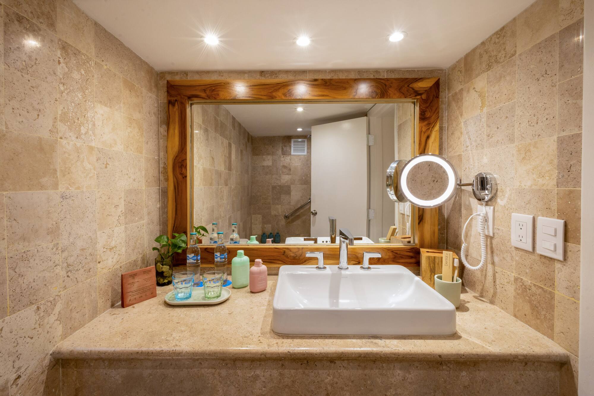 Luxury hotel bathroom with travertine vanity, sleek sink, and illuminated mirror.