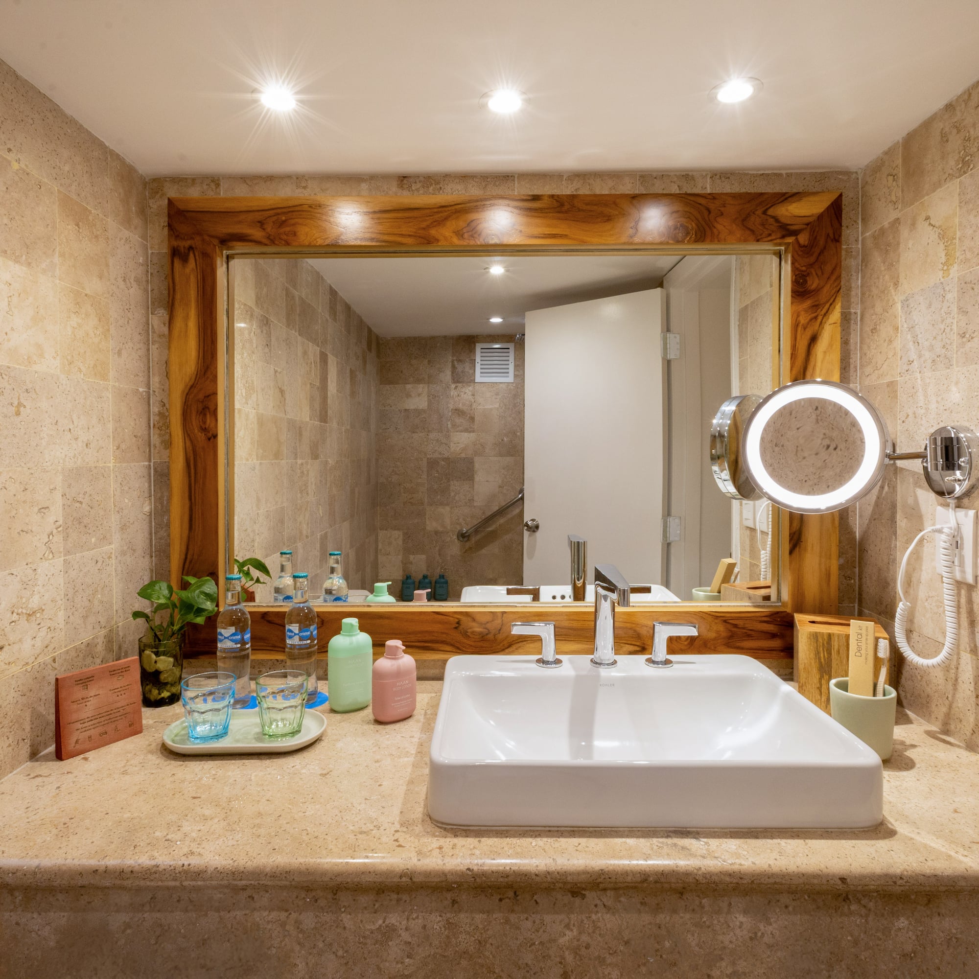 Luxury hotel bathroom with travertine vanity, sleek sink, and illuminated mirror.